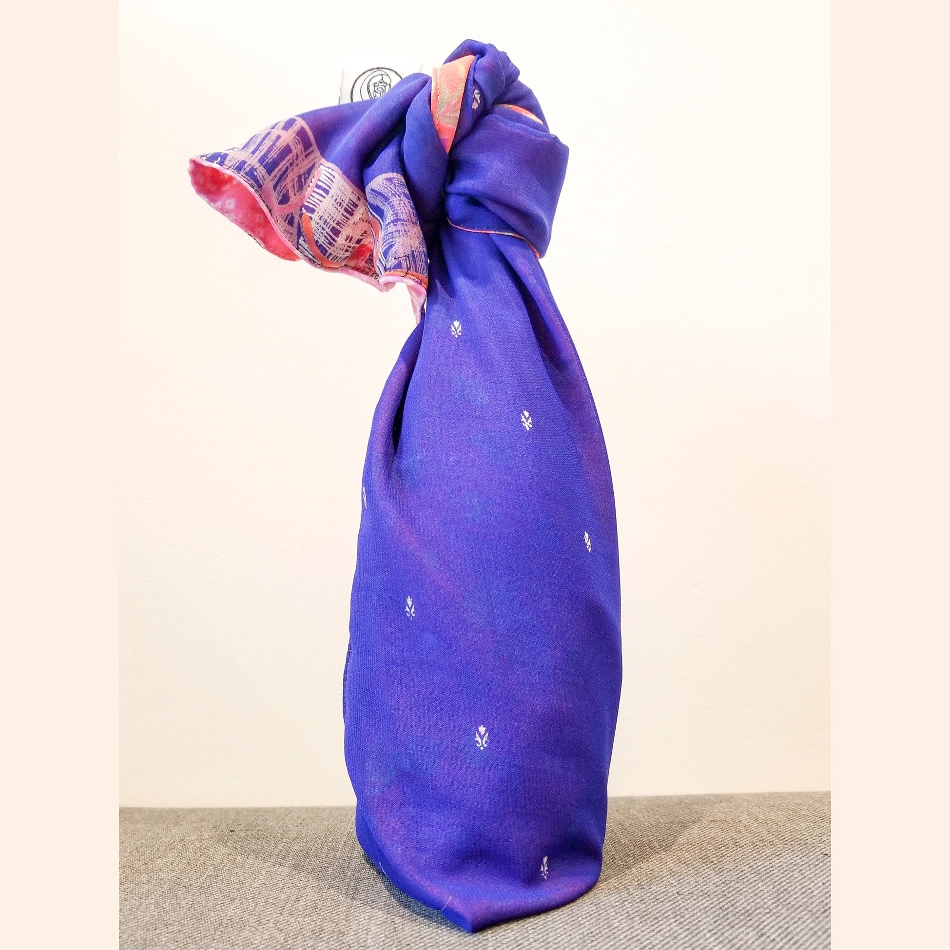 Purple fabric wrapped around a bottle with a decorative pattern on a beige background