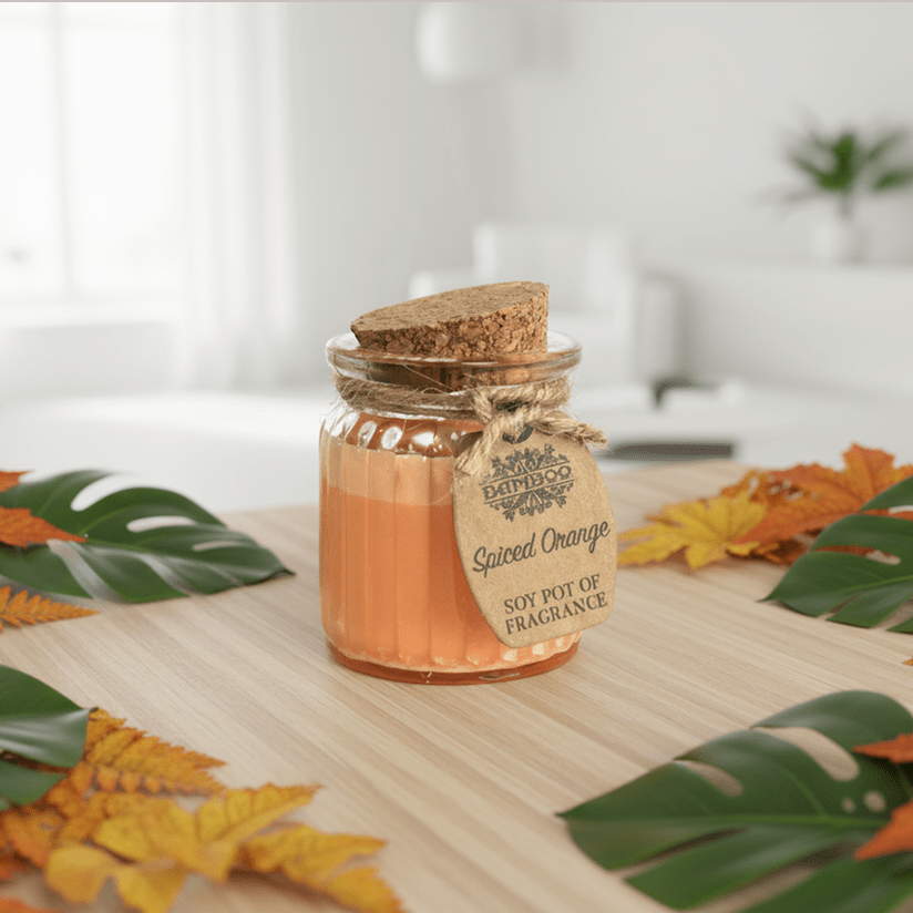 Scented candle in a decorative jar with autumn leaves on a wooden surface