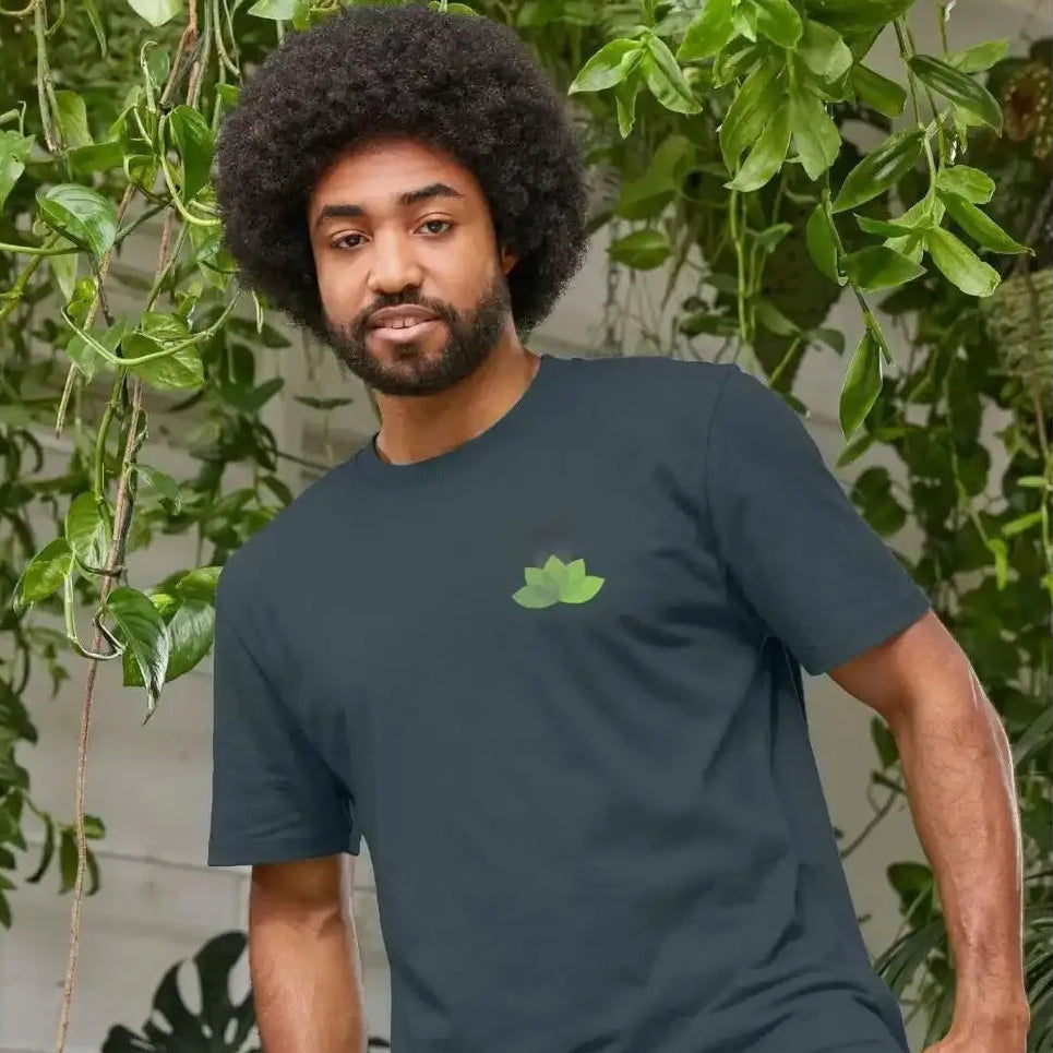 A man wearing a dark green T-shirt with a small logo, standing in front of green plants.