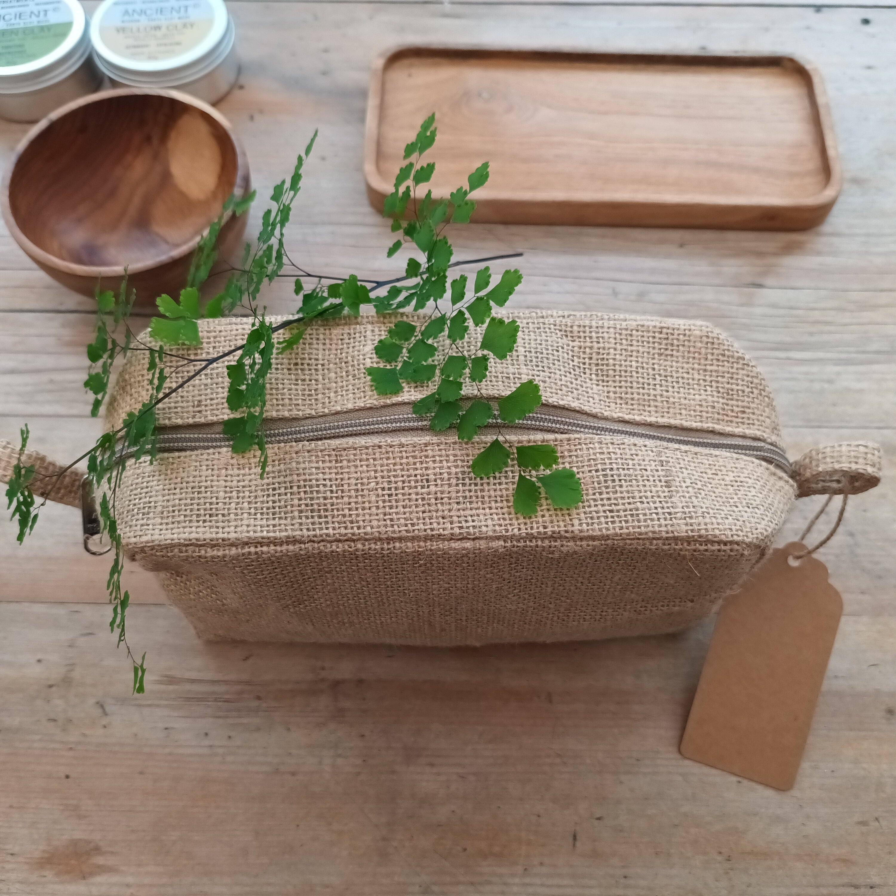 Natural jute washbag with beauty products on a wooden table with green plants