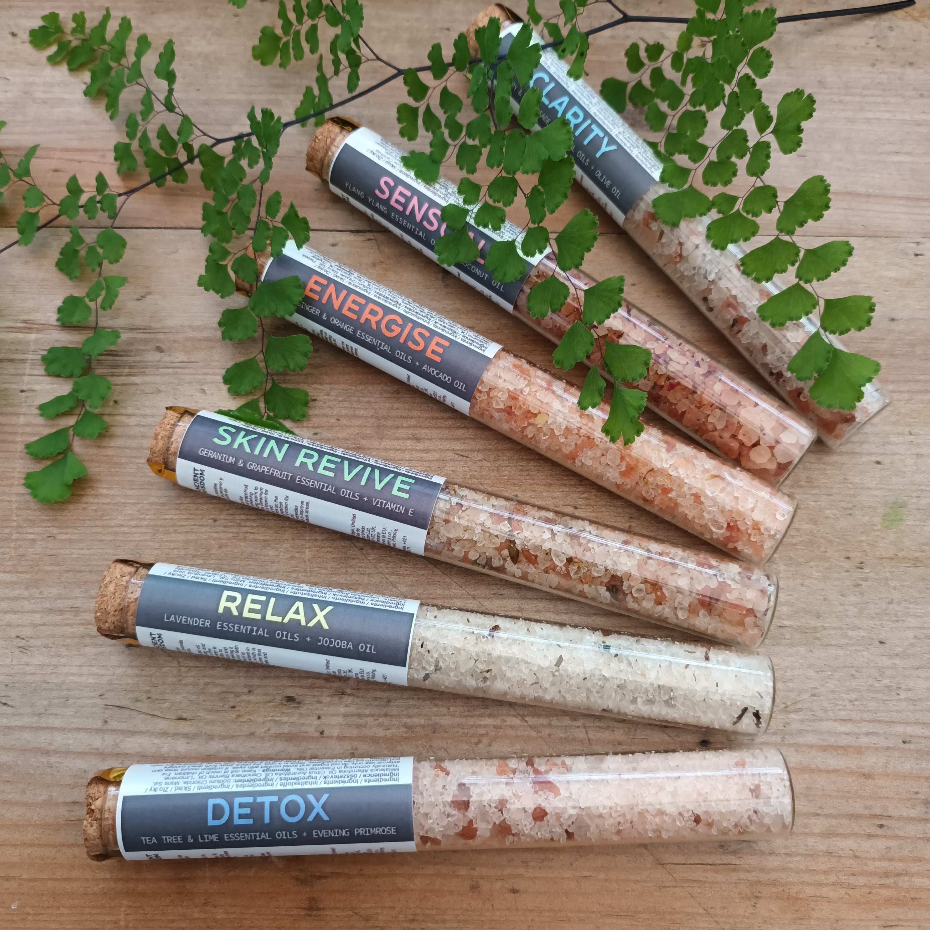 Himalayan bath salt vials on a wooden background with green leaves