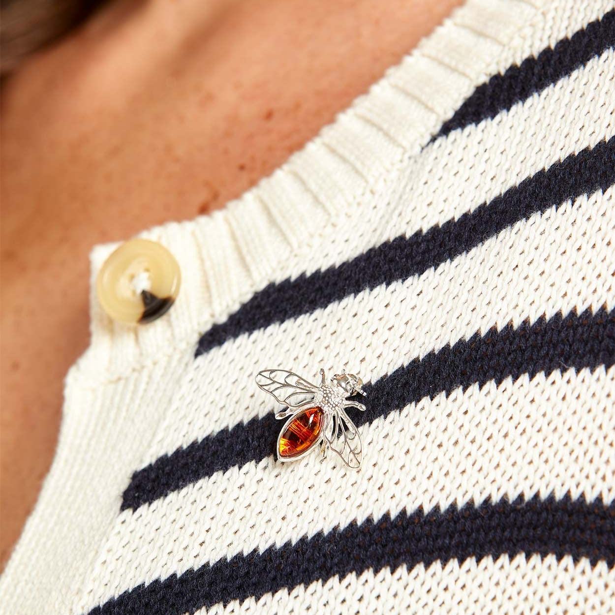Close-up of a person wearing a white and navy striped sweater with a decorative insect pin.