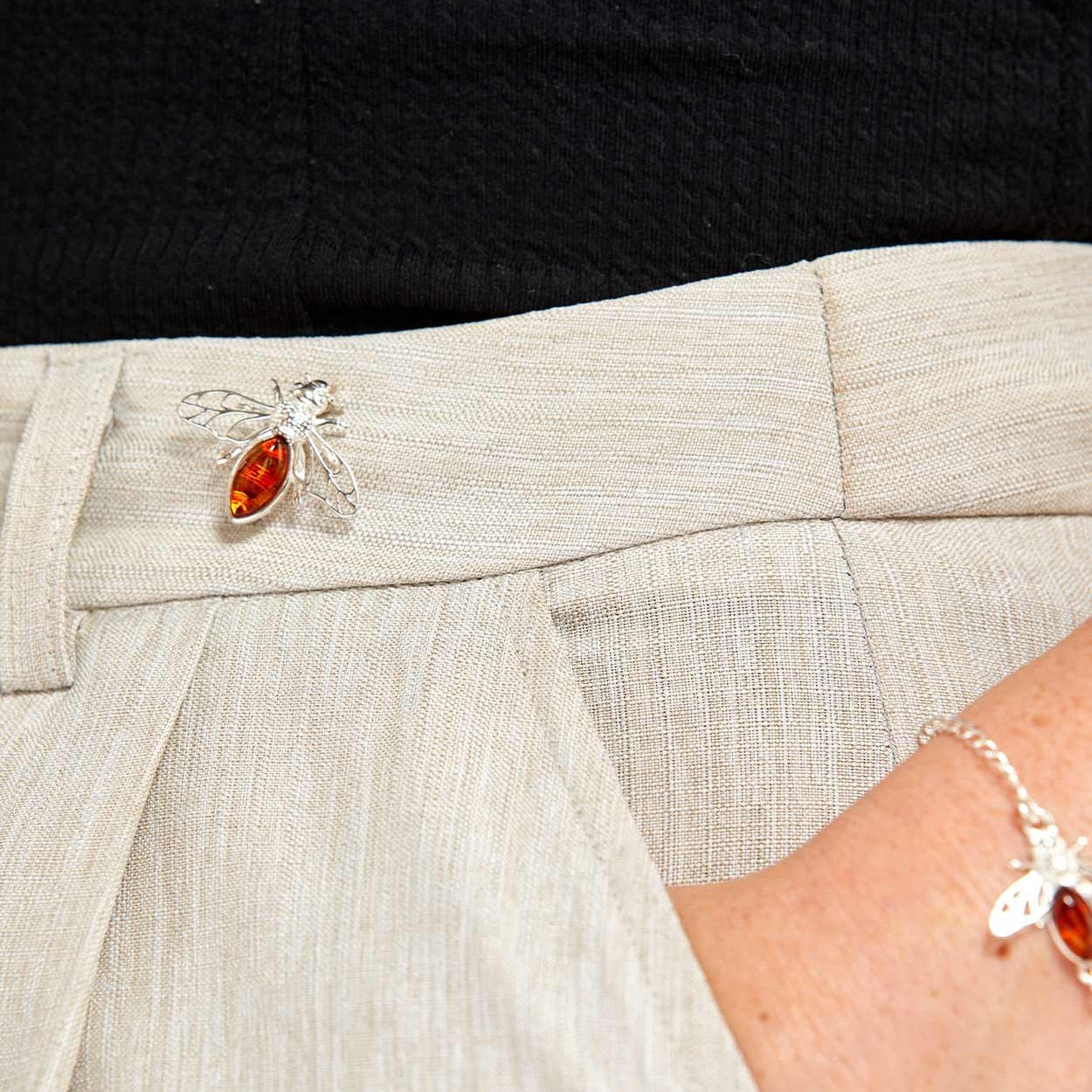 Close-up of a person wearing a silver bee brooch with an orange gemstone on a light-colored garment.