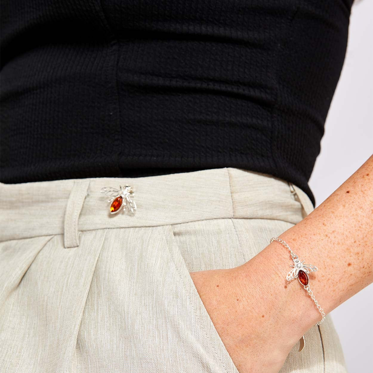 Person wearing a silver bee bracelet with amber gemstones on a plain background