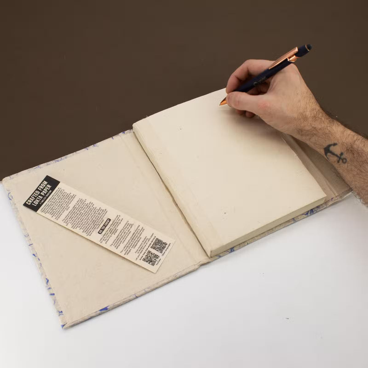 Hand writing in an open notebook with a pen on a white surface.