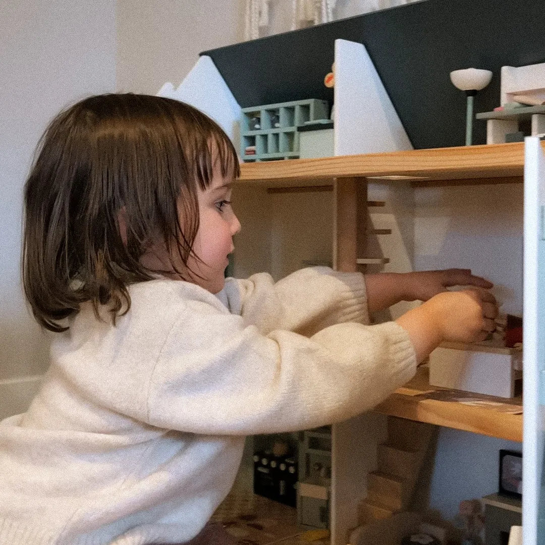 Child playing with a toy kitchen set in a room with furniture and decor.