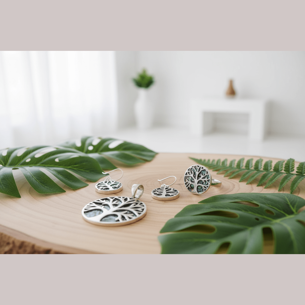 Silver tree-themed earrings on a wooden surface with green leaves