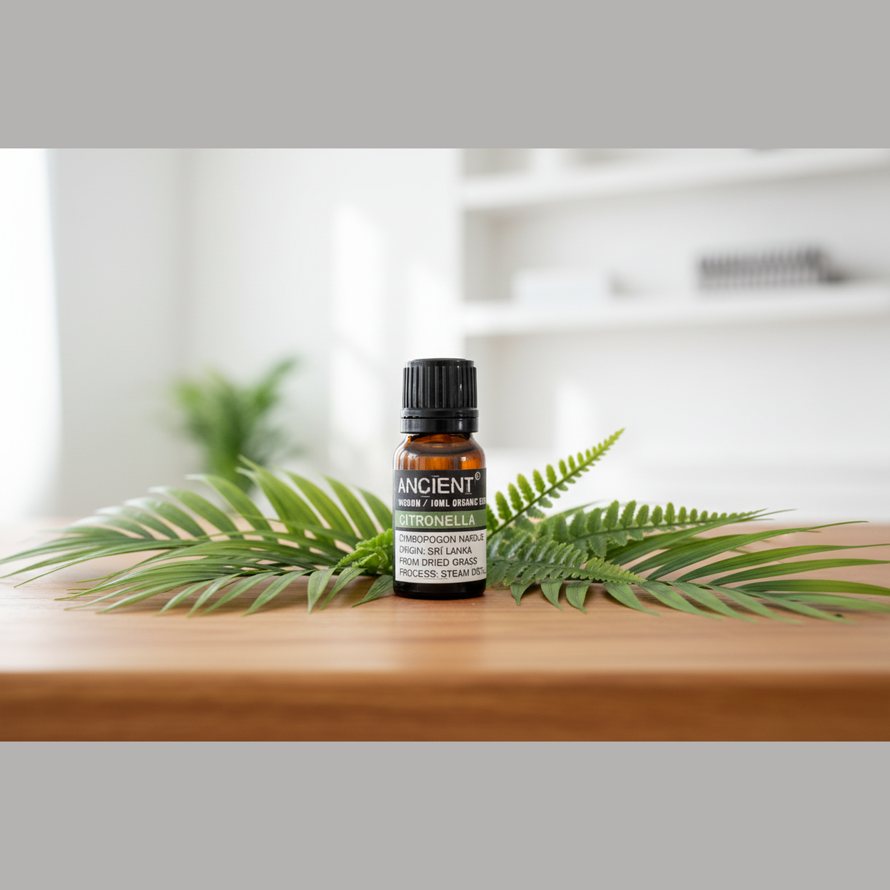 Bottle of essential oil labelled 'Ancient Wisdom' on a wooden surface with fern leaves.