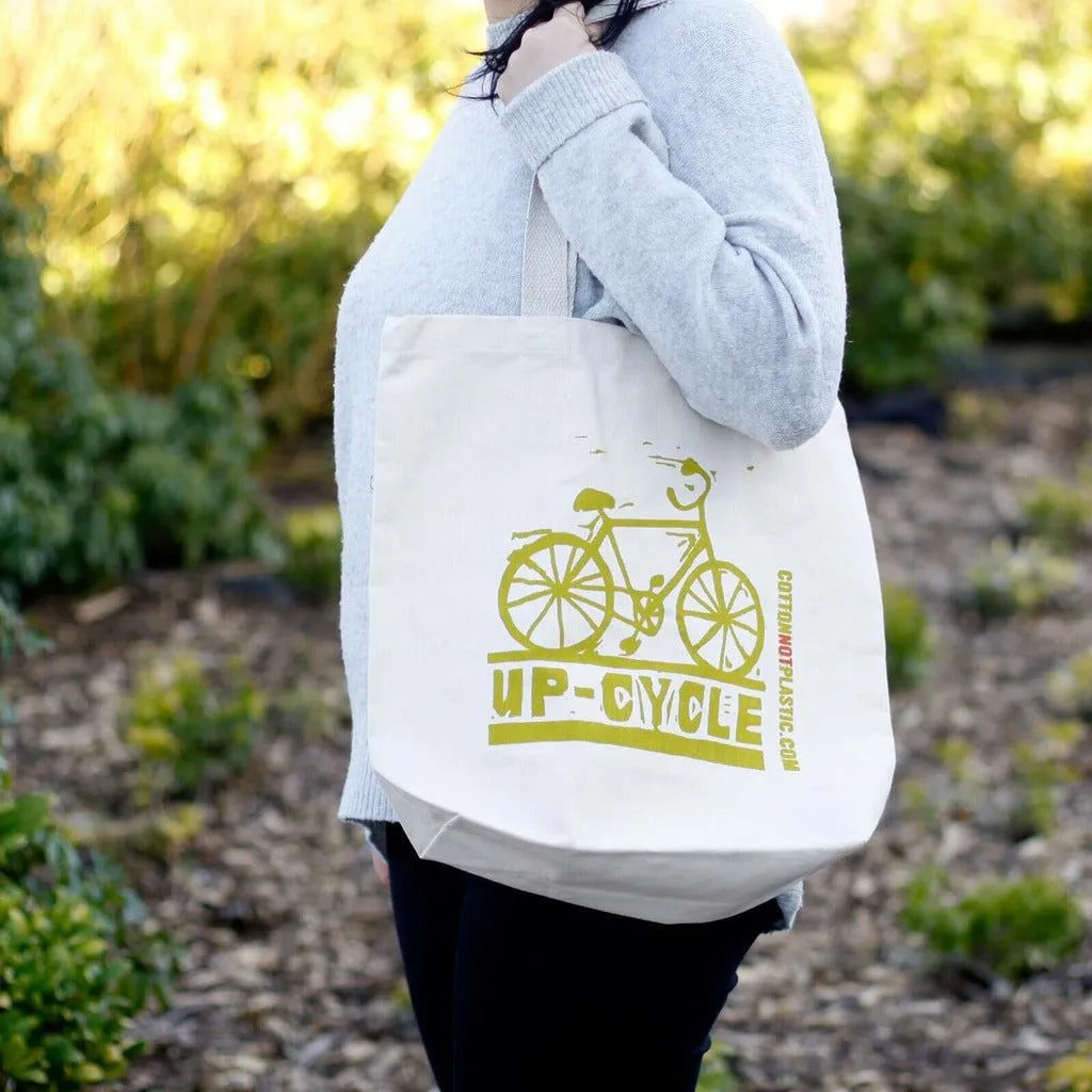 Person holding a cotton tote bag with a bicycle design and 'UP-CYCLE' text outdoors.