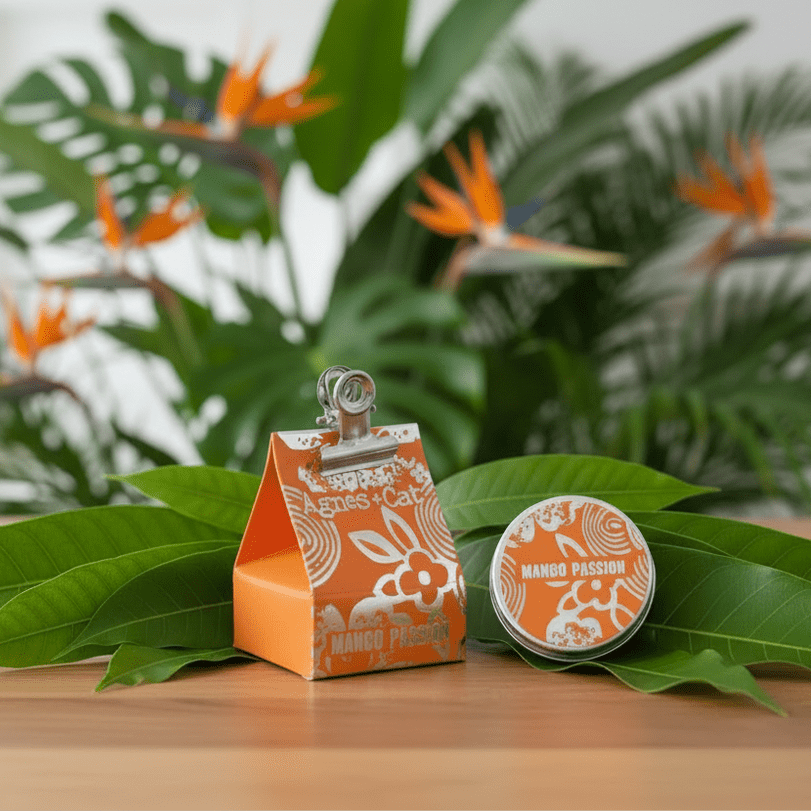 Orange and white Natural lip balm packaging with a clip on a wooden surface with green leaves and plants in the background