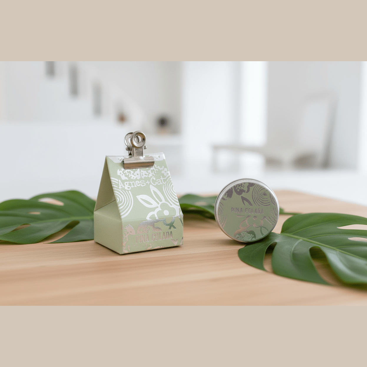 Small green box with a clip on top, next to a natural lip balm, on a wooden surface with leaves.