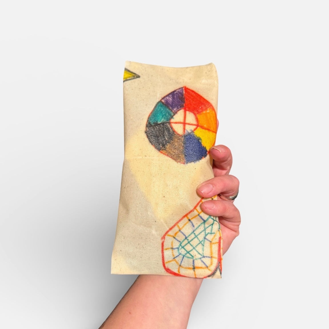 Hand holding a colorful embroidered fabric with geometric patterns on a plain background