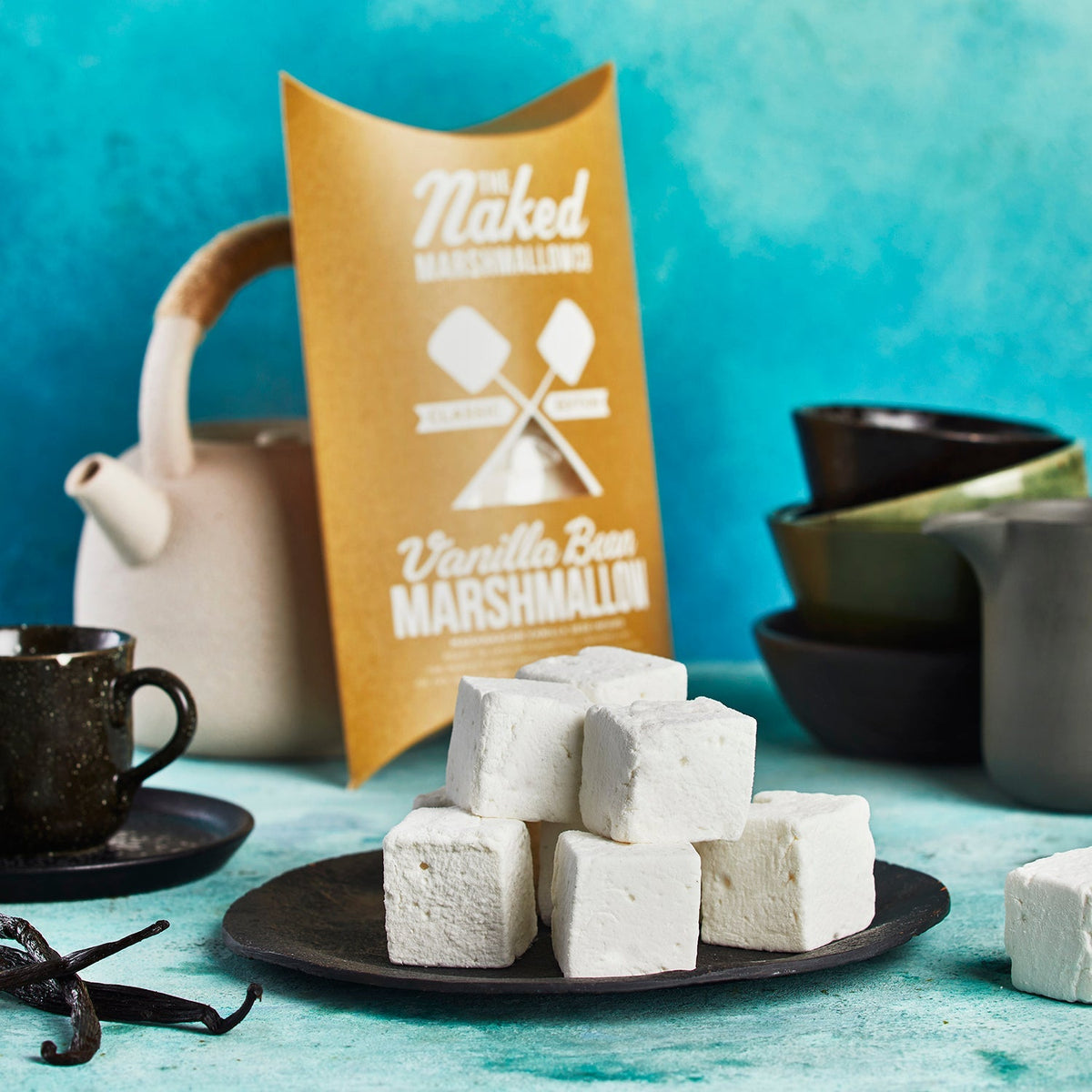 Naked Vanilla Bean Marshmallows on a plate with packaging and teaware in the background.