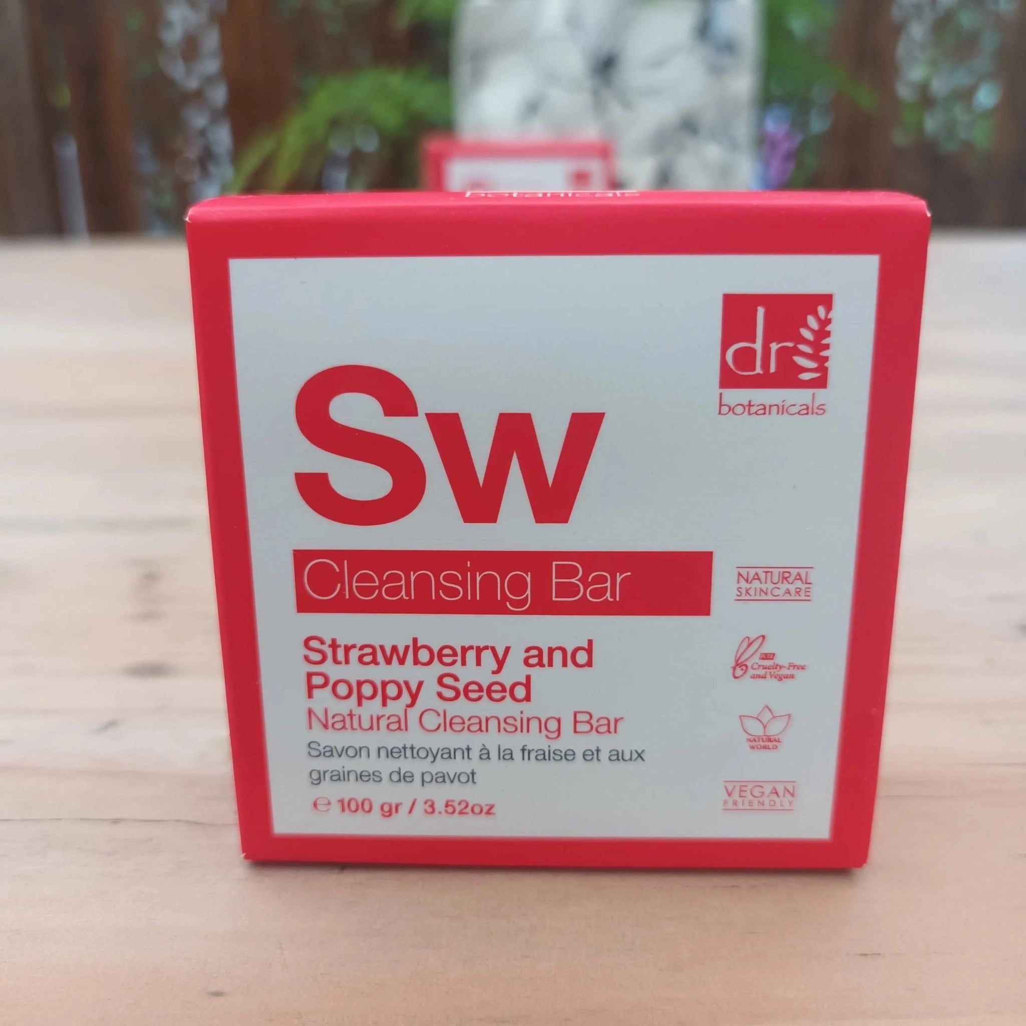 Red and white box of Strawberry and Poppy Seed Cleansing Bar on a wooden surface