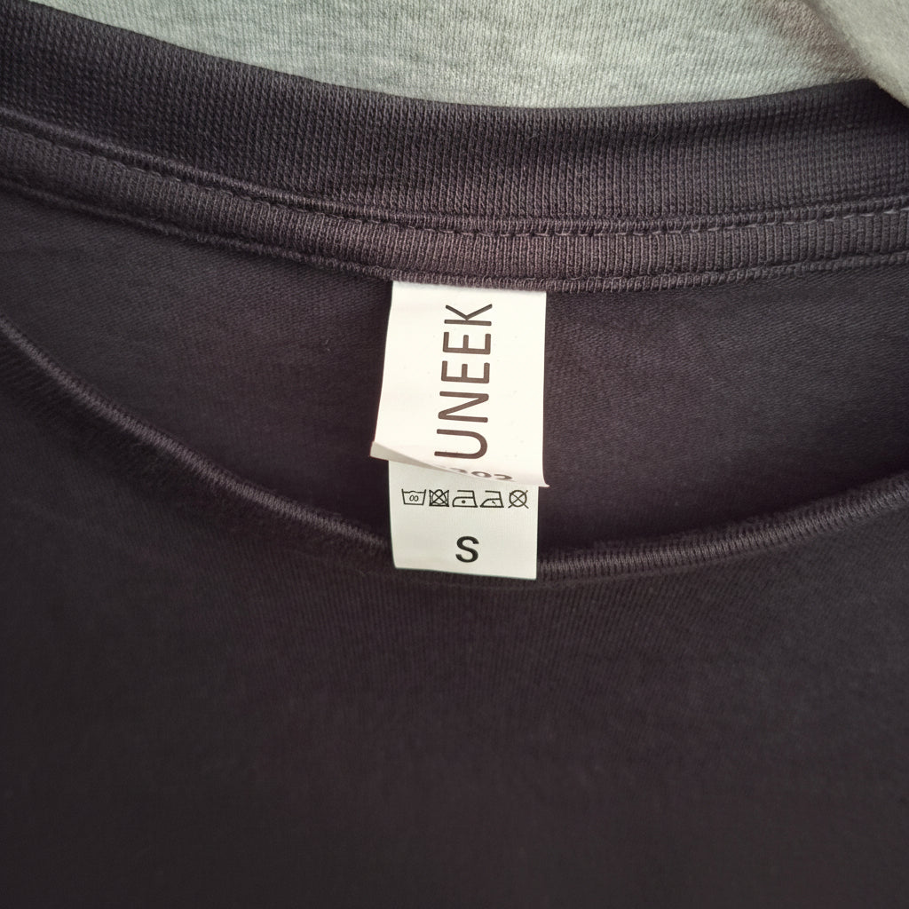 Close-up of a small man's Blac t-shirt with a 'UNEEEK' label on a dark background