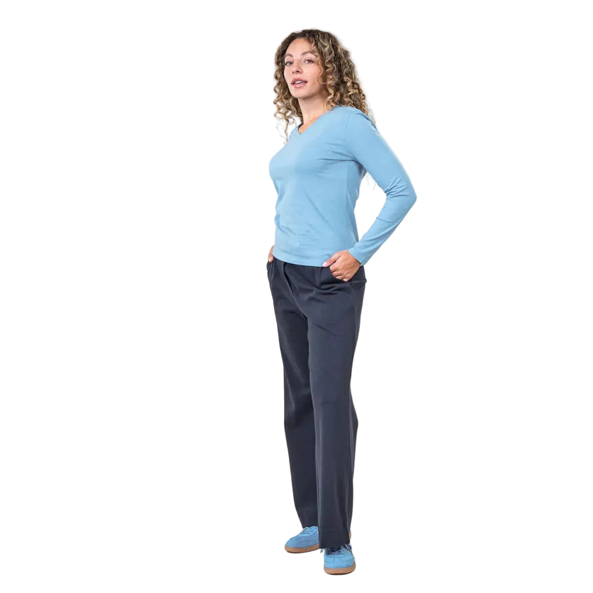 Woman wearing a blue long-sleeve top and dark pants on a white background