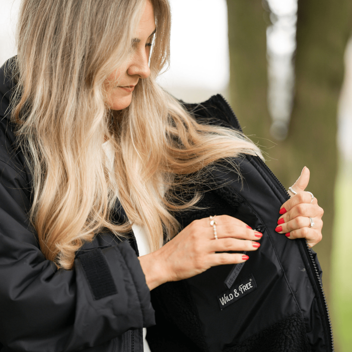Woman wearing a black jacket with 'Wild & Free' branding, outdoors.