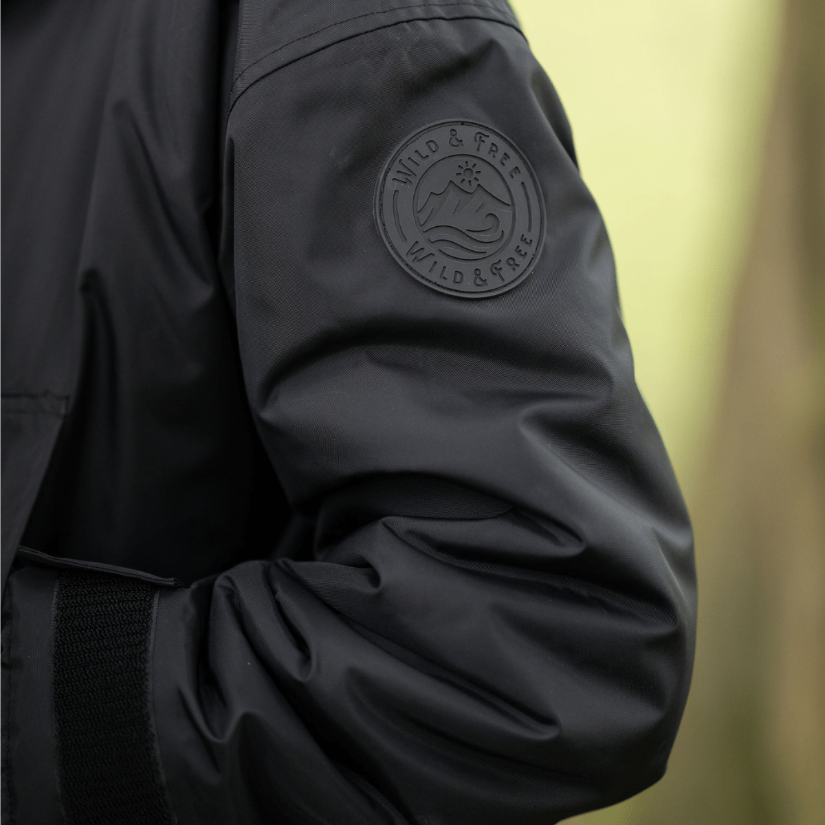 Black jacket with a visible brand logo on the sleeve against a blurred natural background