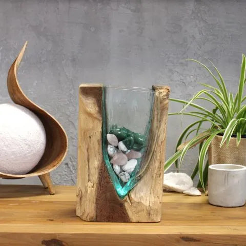 V-shaped glass vase containing decorative stones, displayed beside a potted plant.