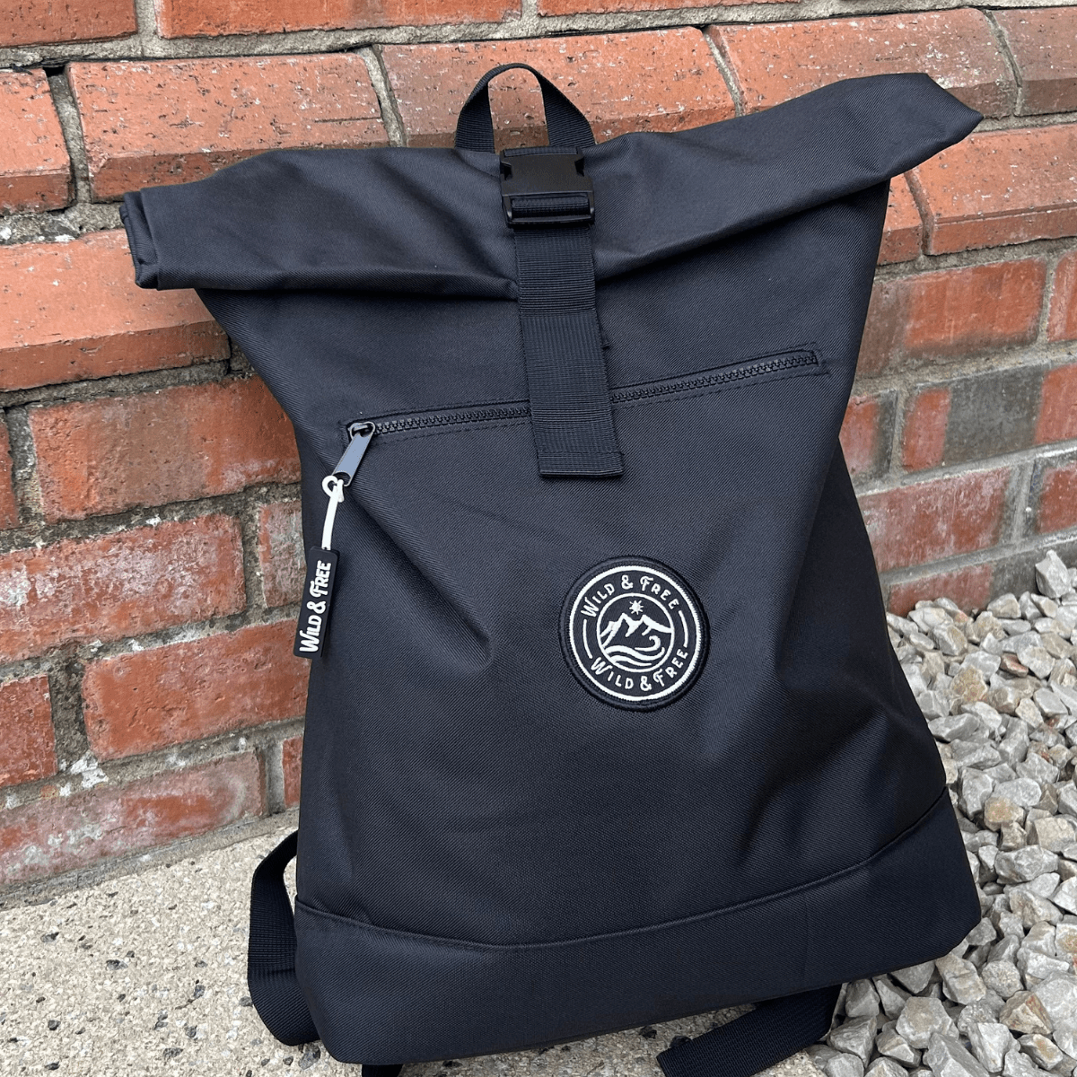 Black backpack with a logo against a brick wall background