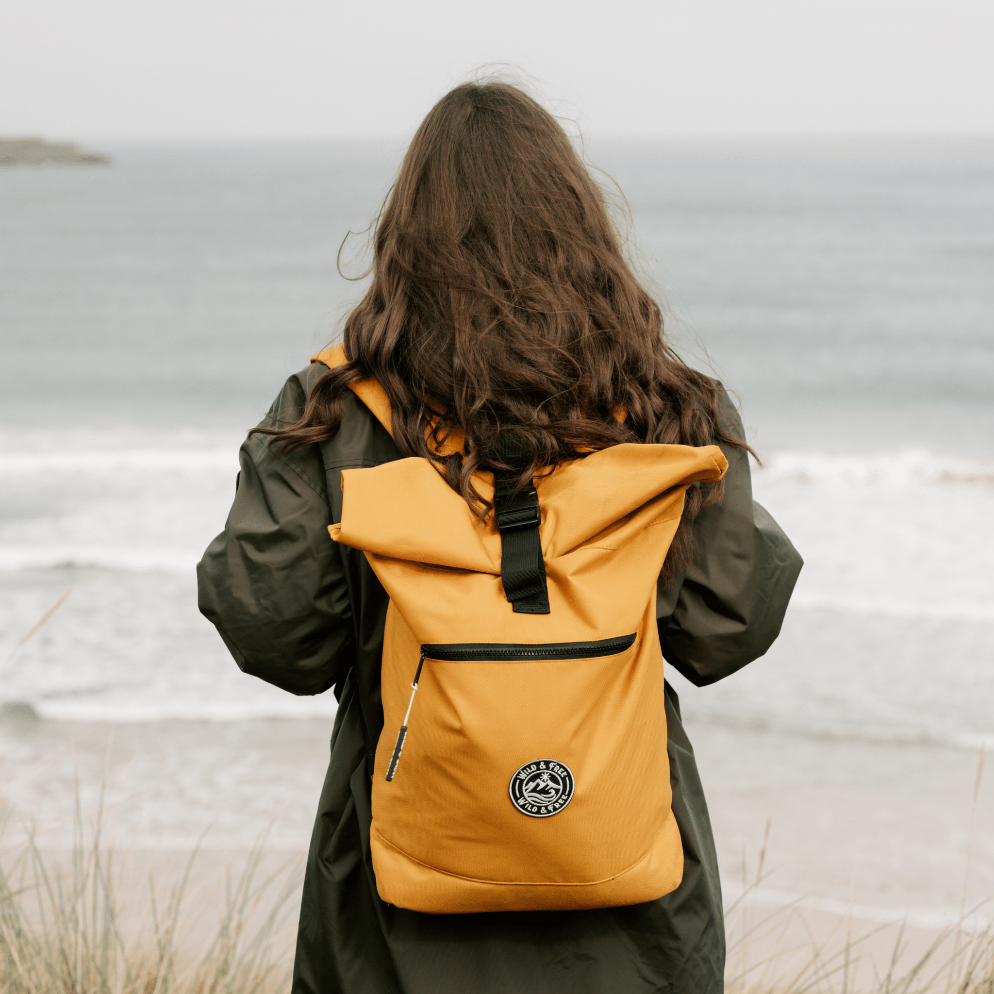 Person wearing a yellow backpack with a logo, standing by a body of water.