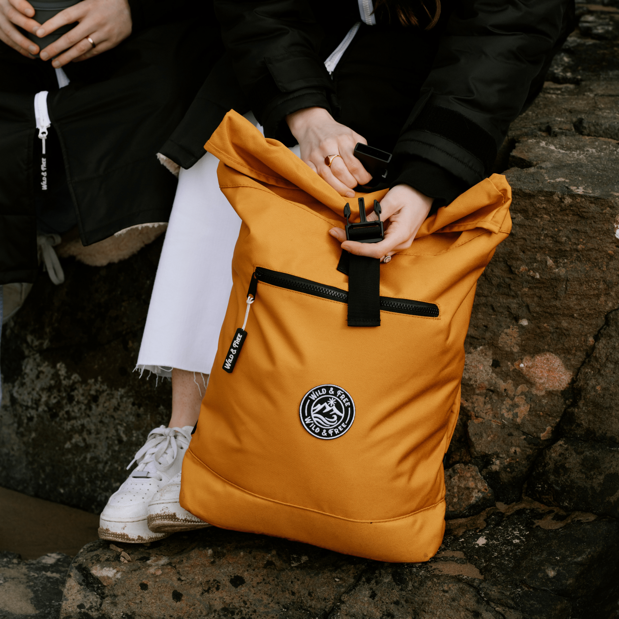 Person sitting on a stone wall with an orange backpack featuring a logo.