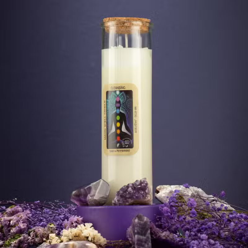 A glass jar candle with a cork stopper and cream-colored wax stands on a purple pedestal surrounded by purple crystals and dried lavender flowers against a dark blue background. The front label reads 'CHAKRA' and 'CHAKRA ENERGizing candle'.