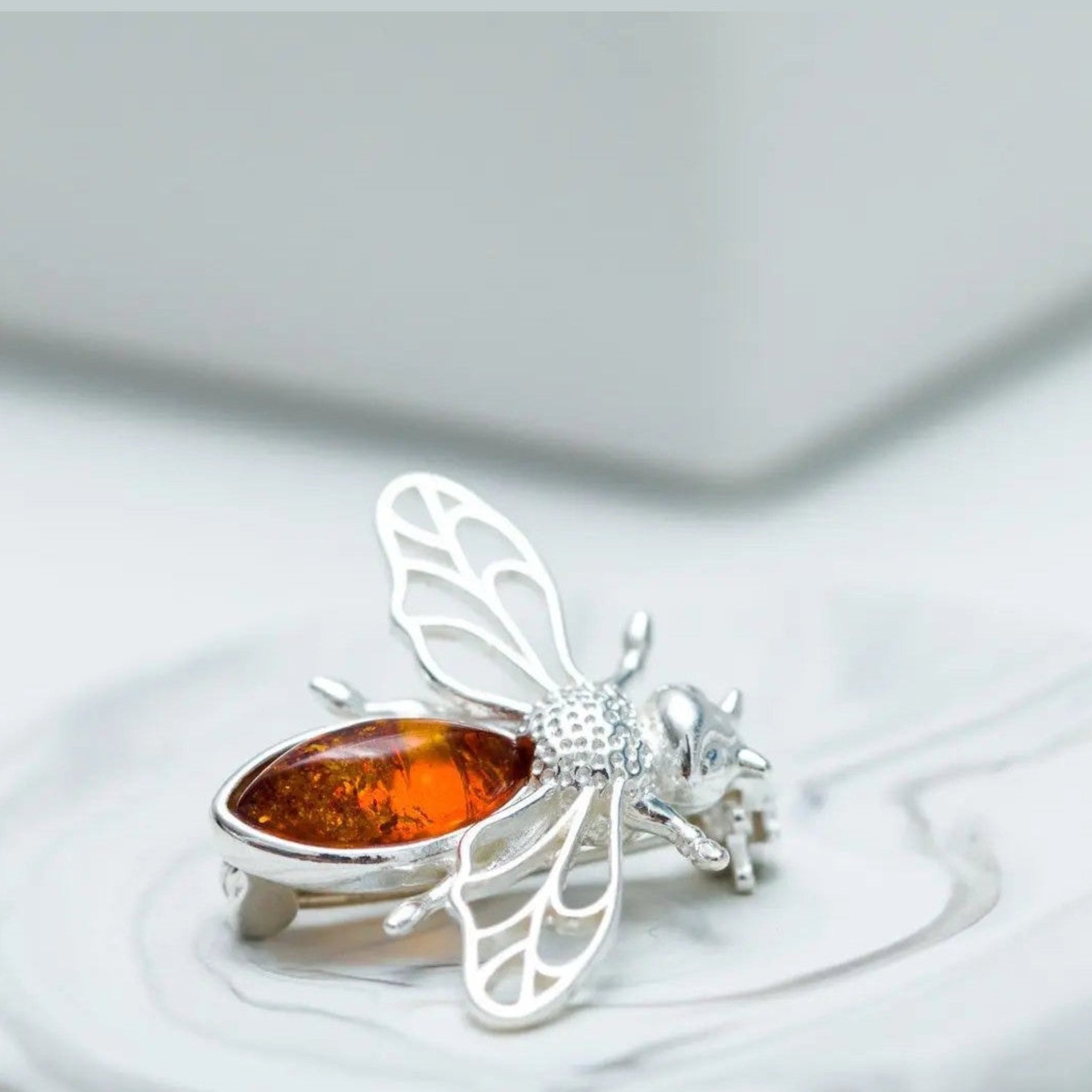 Silver butterfly brooch with amber stone on a white stone surface