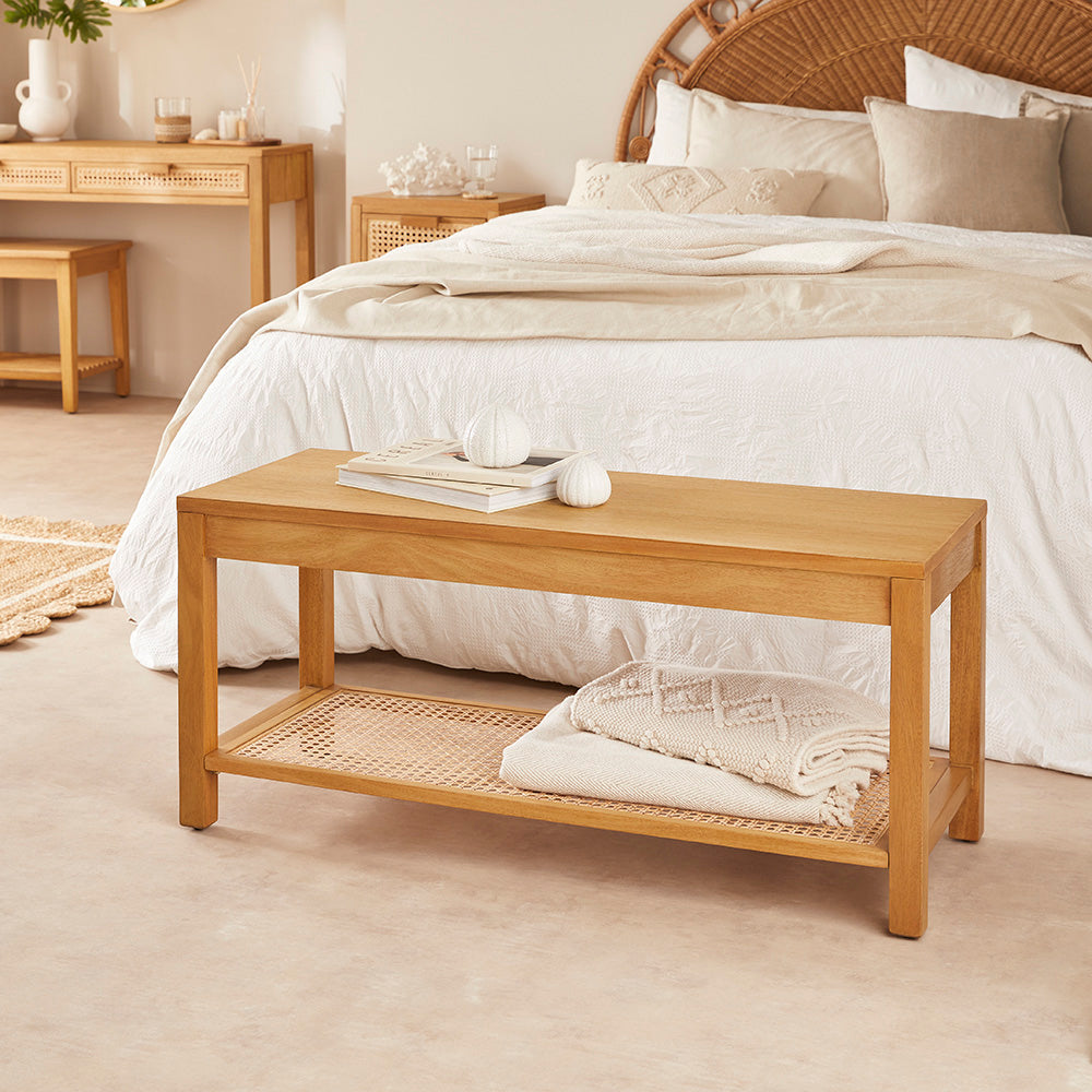 Wooden bench in front of a bed with white bedding and a wicker headboard.