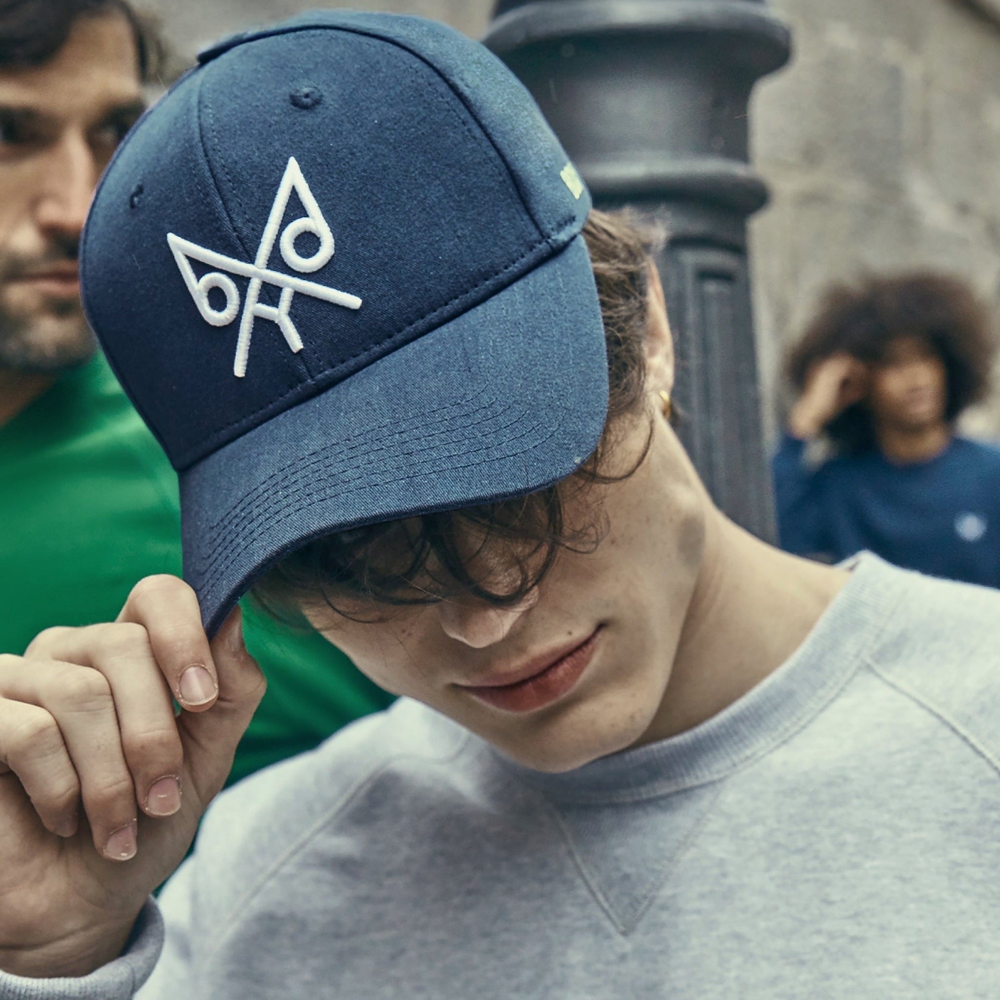 Person wearing a blue cap with a logo, standing outdoors with blurred people in the background