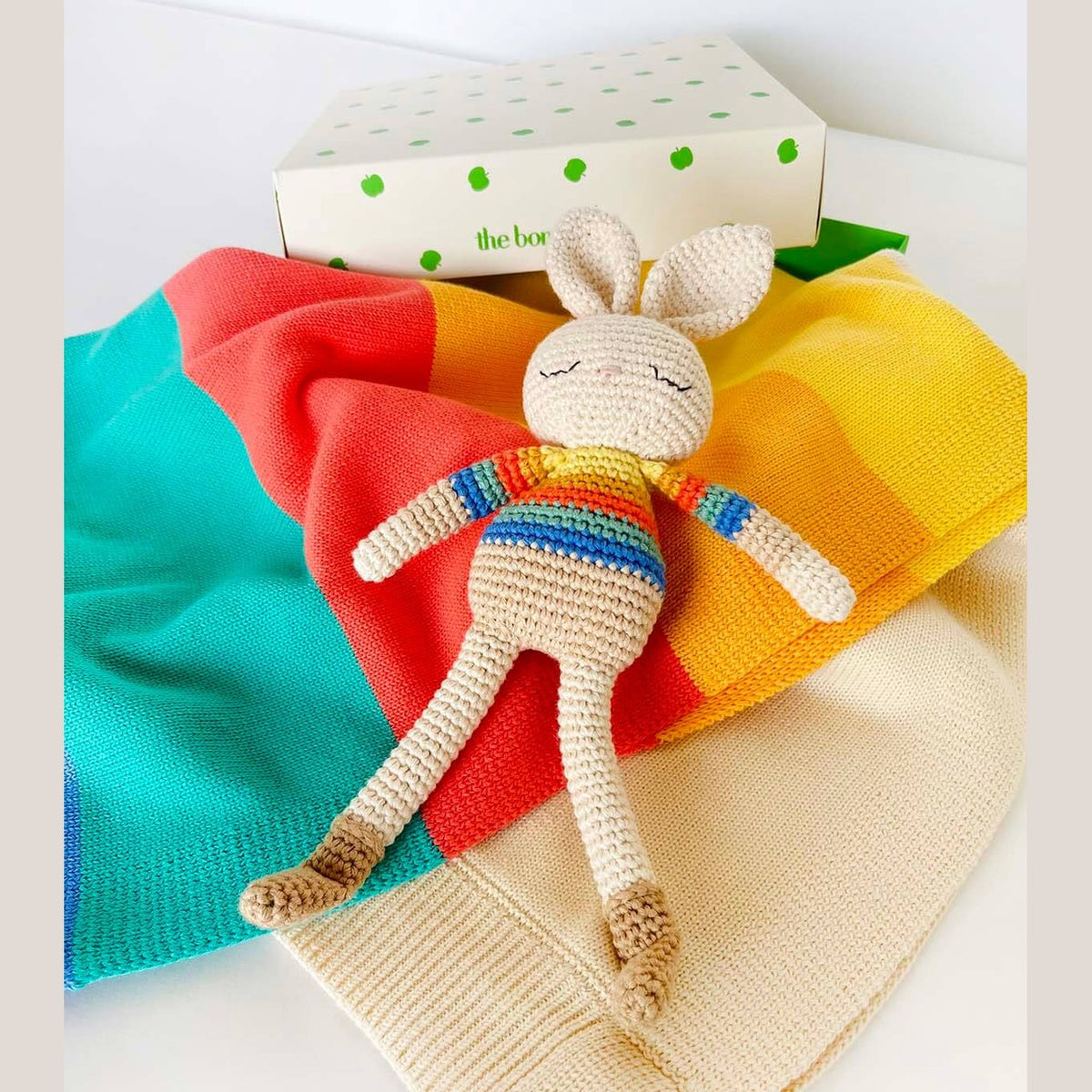 Bonnie Bunny crochet toy resting on rainbow knitwear beside The bonniemob branded box