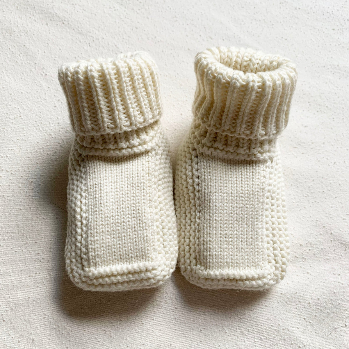 Pair of white knitted baby booties on a light background