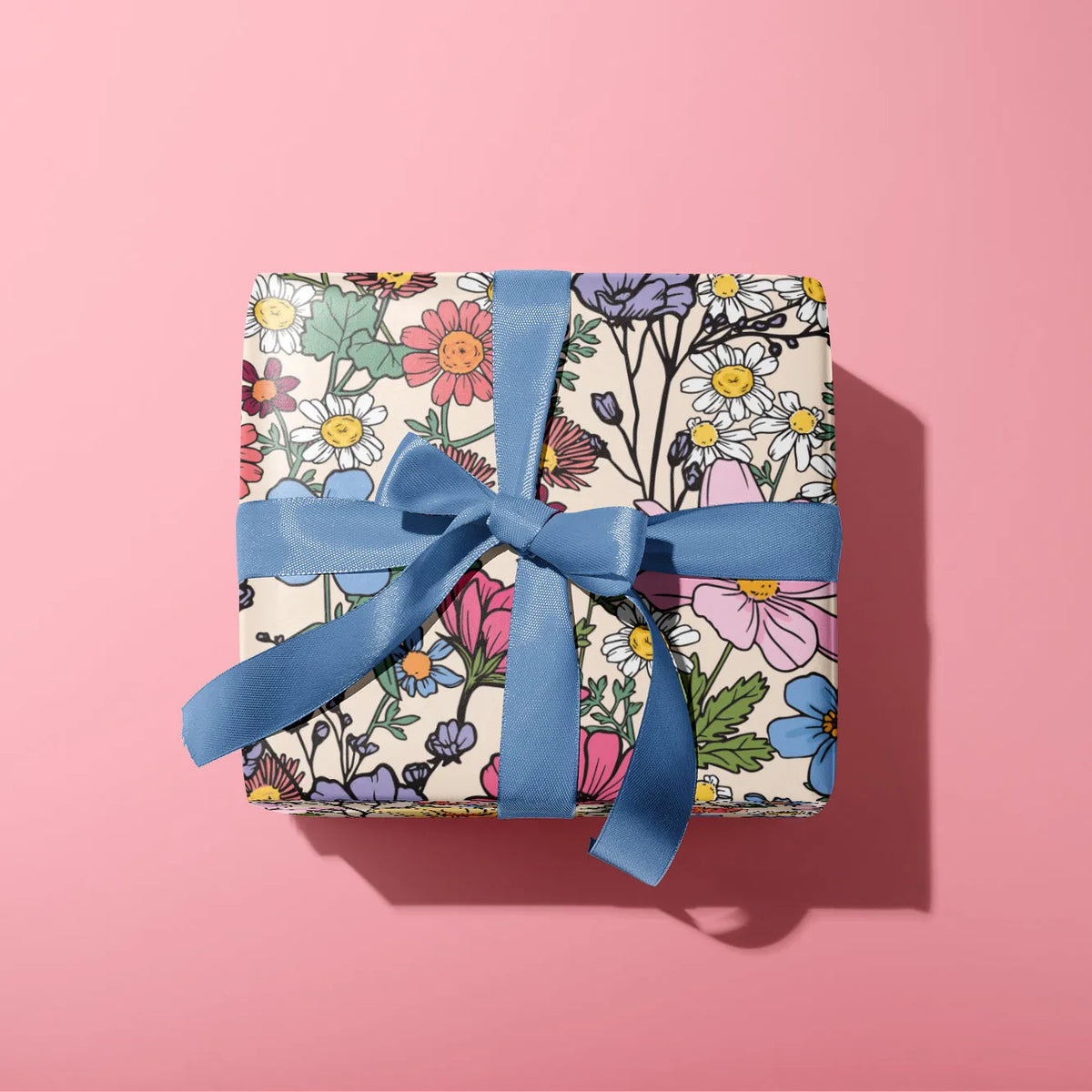 Gift wrapped in paper with floral pattern and blue ribbon on a pink background