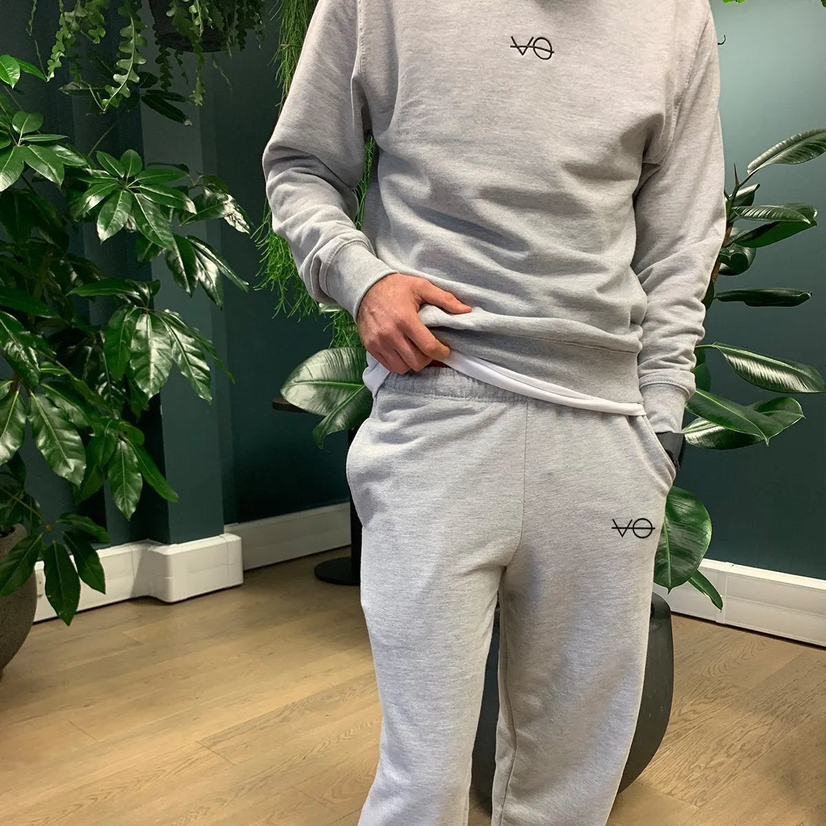 Person wearing a gray tracksuit with a logo in a room with plants