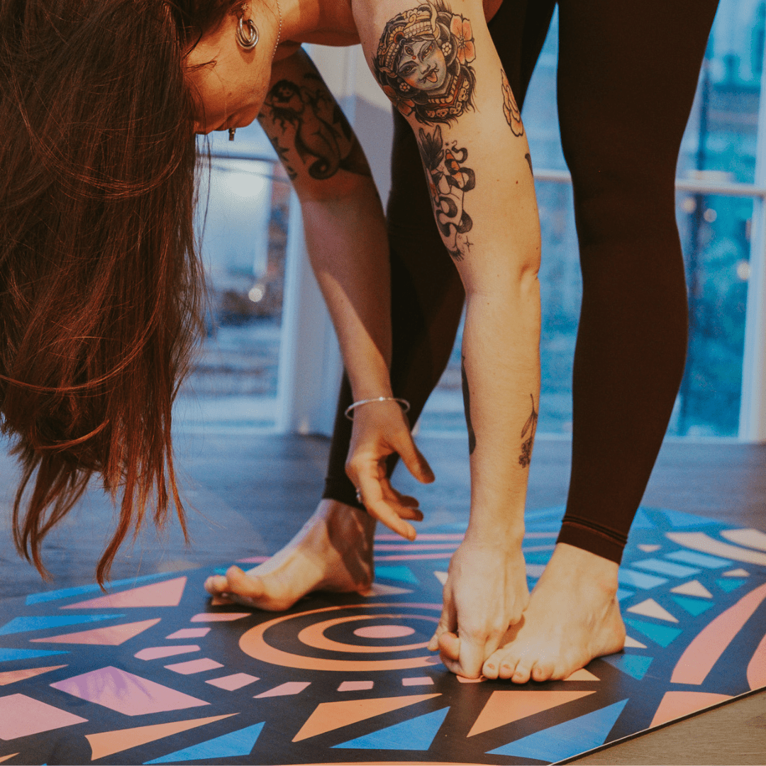 Person stretching on a colorful yoga mat with tattoos visible