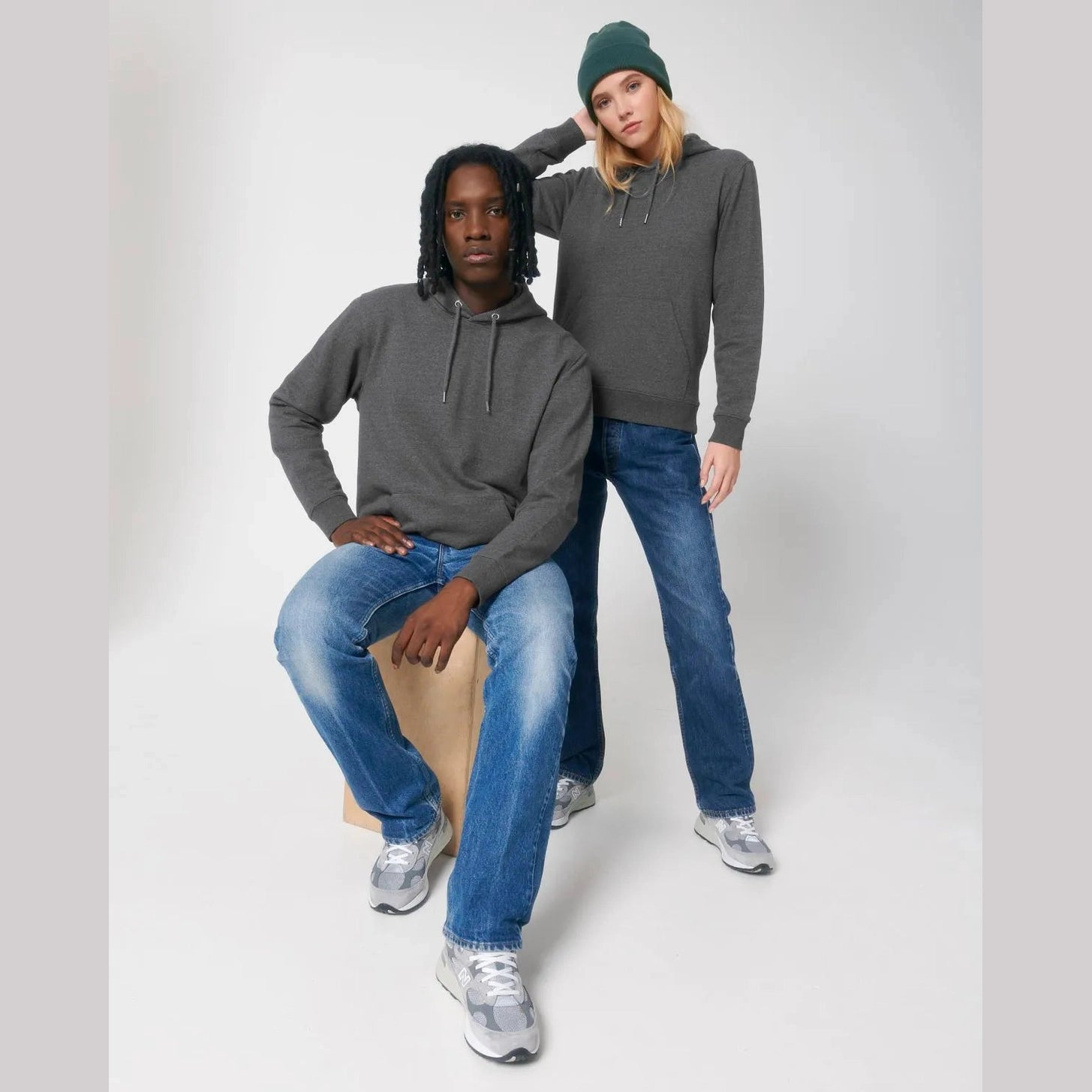 Two people wearing gray hoodies and blue jeans on a white background