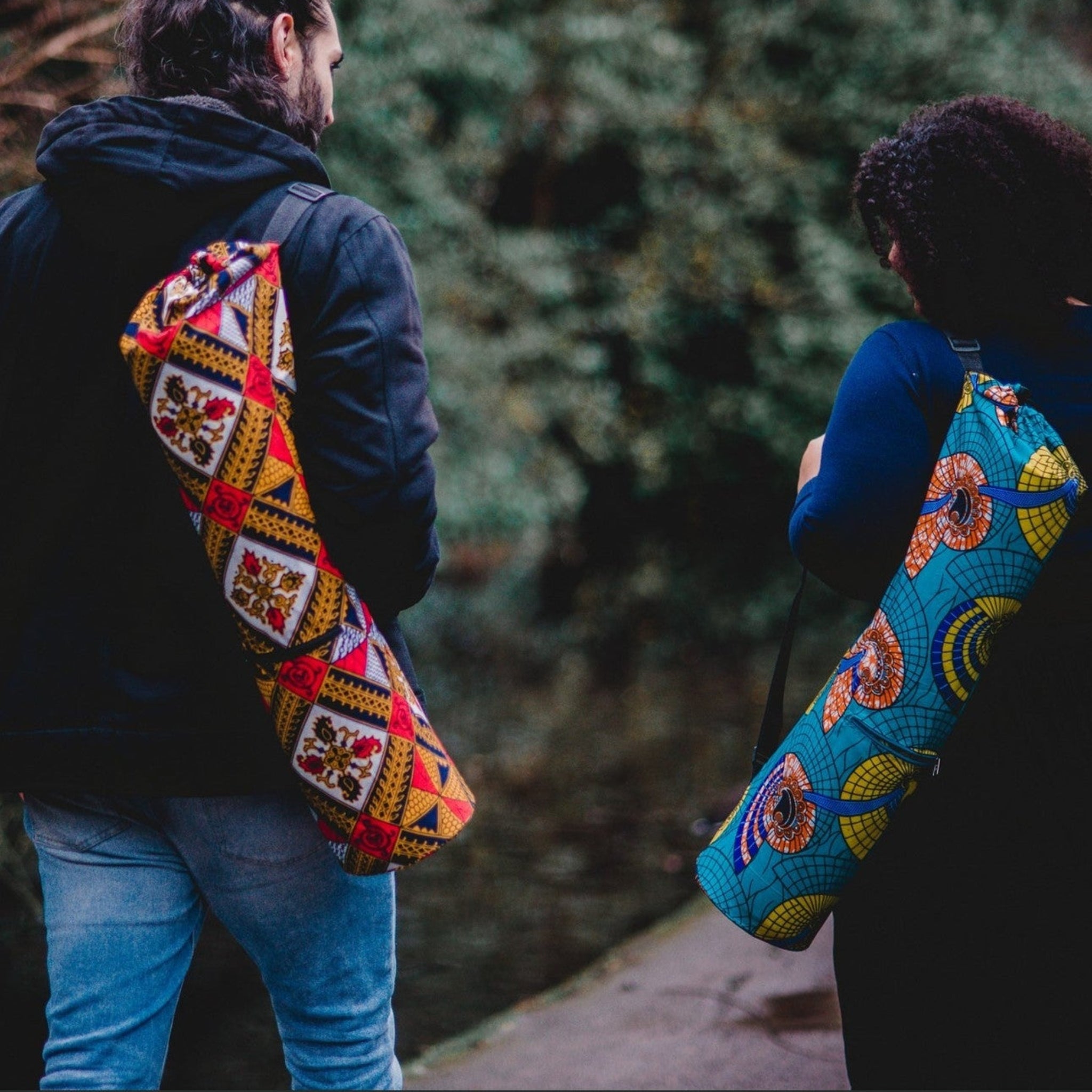 Two people walking outdoors with colourful, patterned yoga bags on their backs.