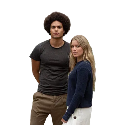 A man and a woman standing against a plain white background. The man has an afro and wears a dark grey t-shirt and brown pants. The woman wears white pants and a recycled navy blue jumper