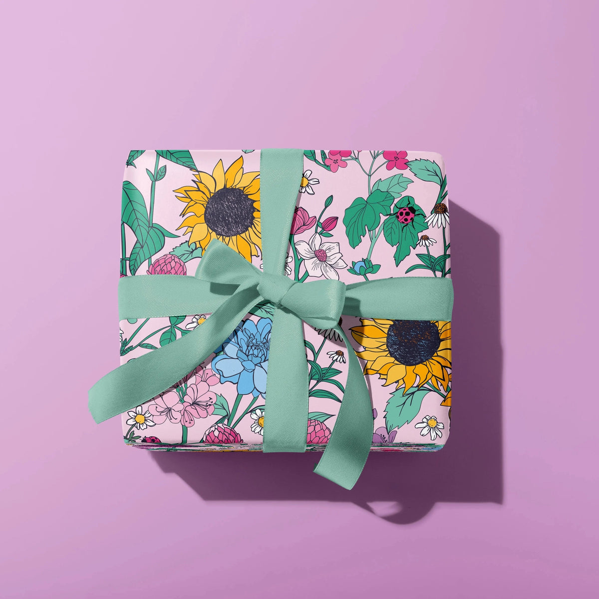 Gift wrapped box with floral pattern and green ribbon on a pink background