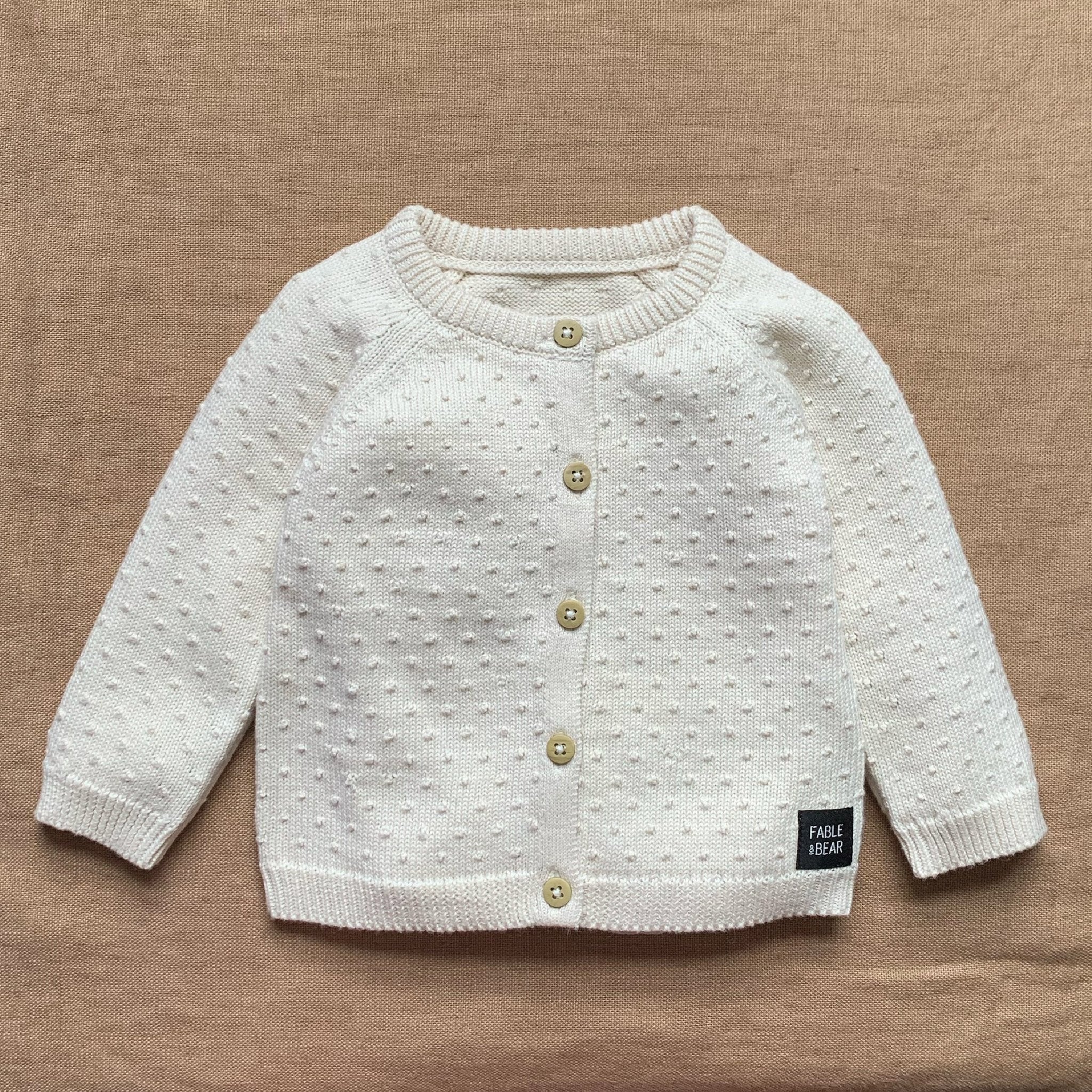 White knitted cardigan with gold buttons on a brown background