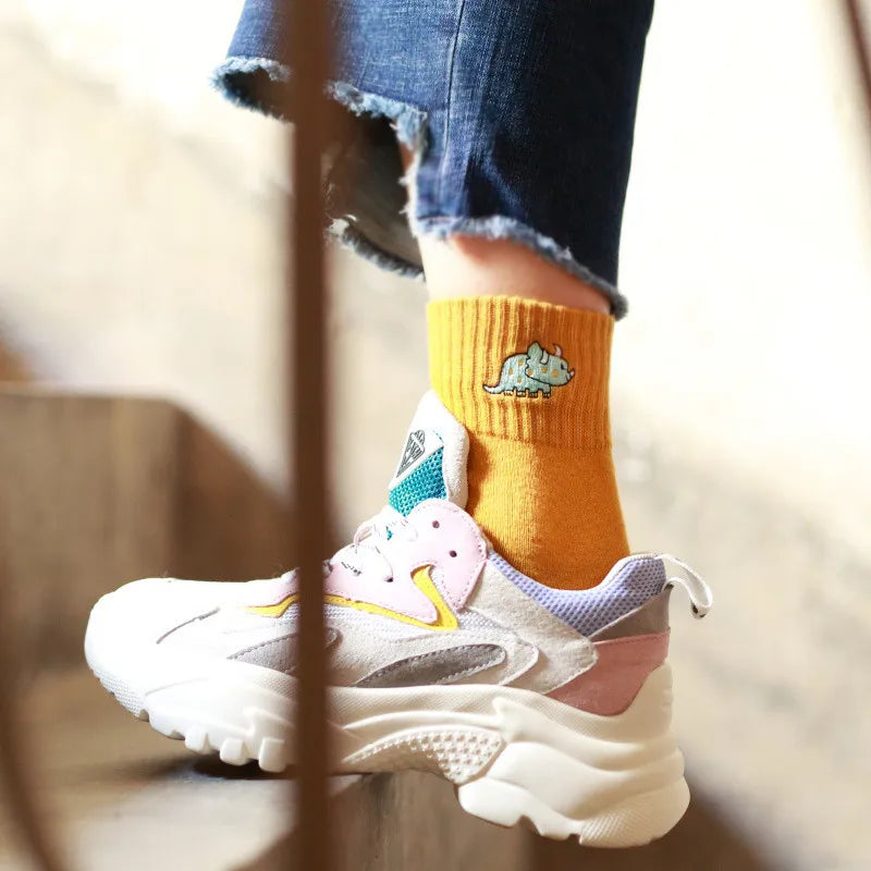 White sneakers with colorful accents worn with mustard yellow socks featuring a green dinosaur design.