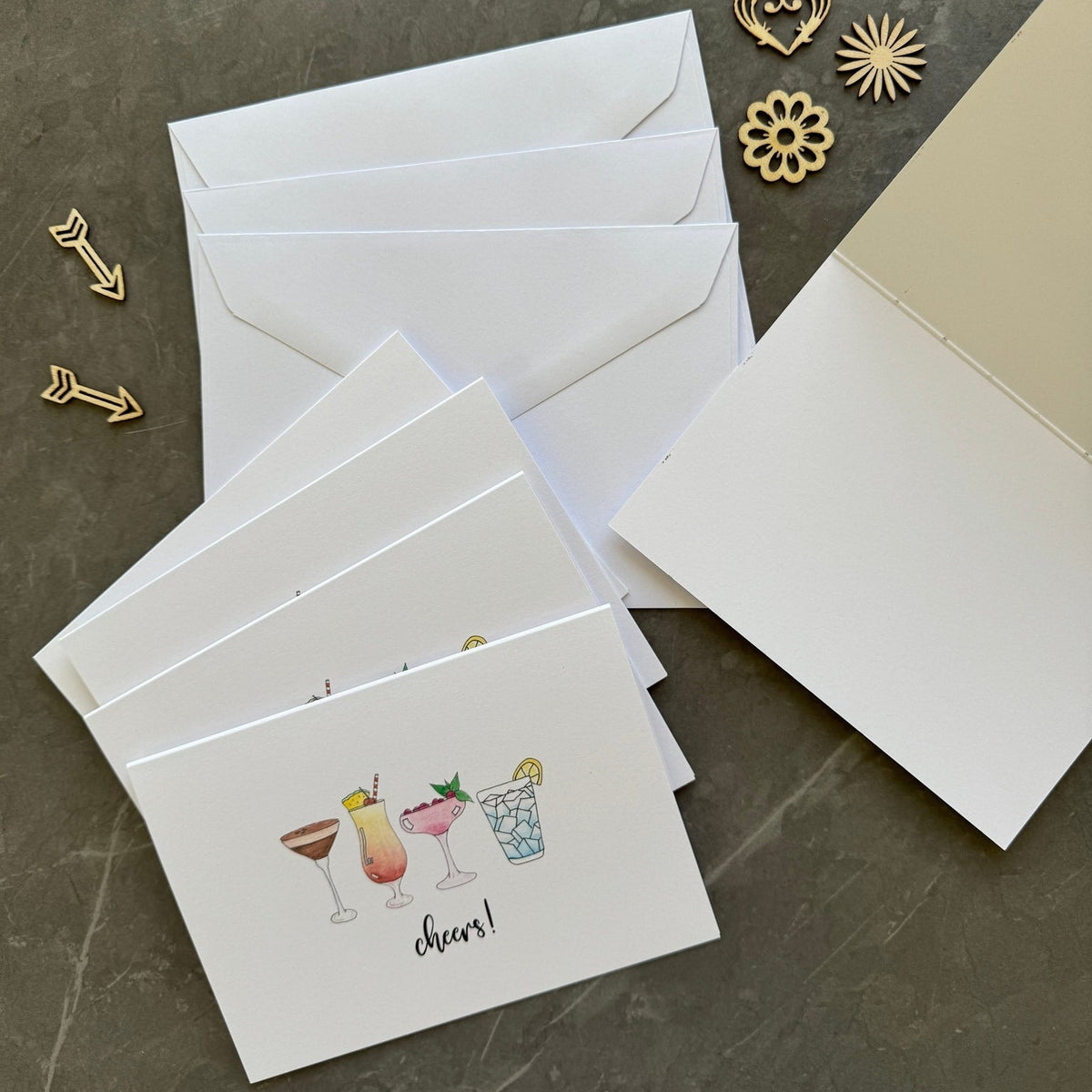 Set of greeting cards with drink illustrations and envelopes on a dark surface.