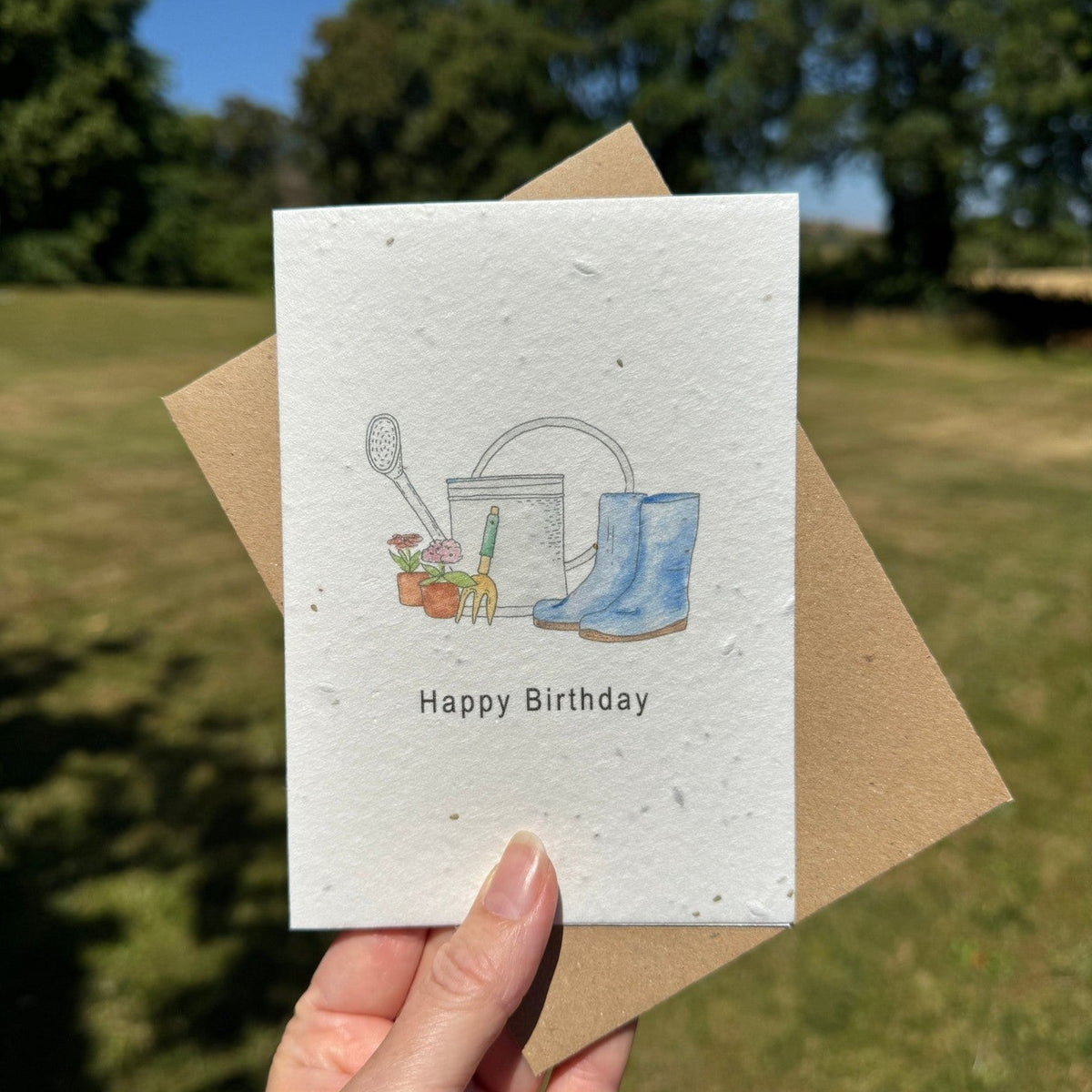 Hand holding a birthday card with gardening illustrations outdoors