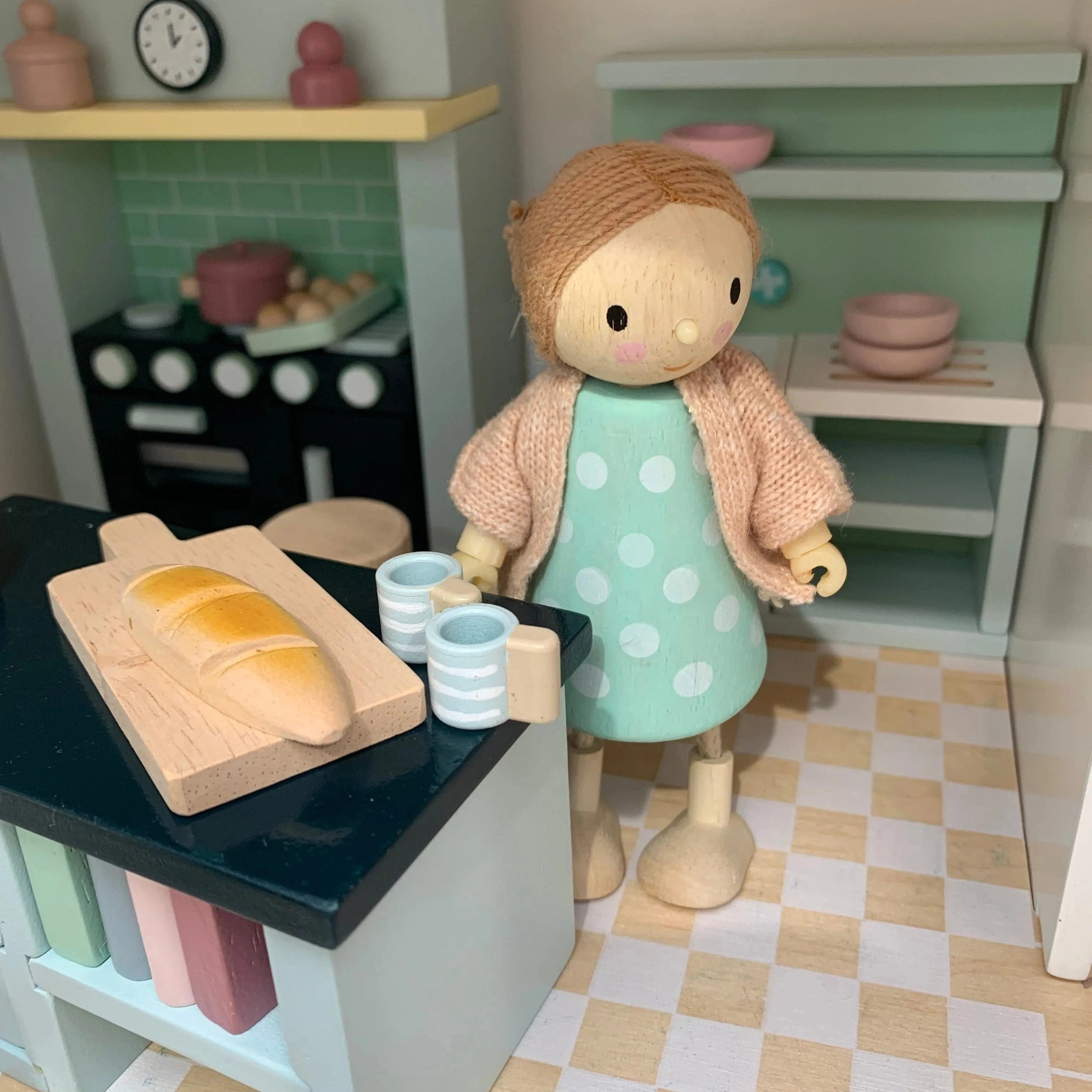 Toy doll in a doll's house  kitchen setting with a loaf of bread and cups on a counter.