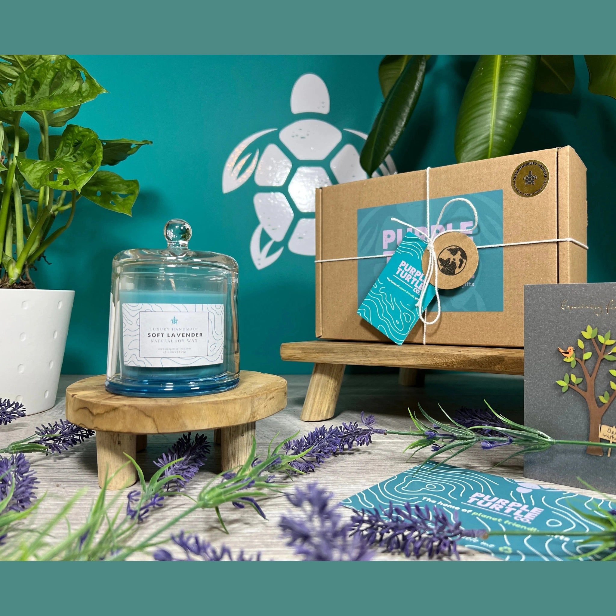 Candle on a wooden stand with a box, card, and lavender flowers on a teal background