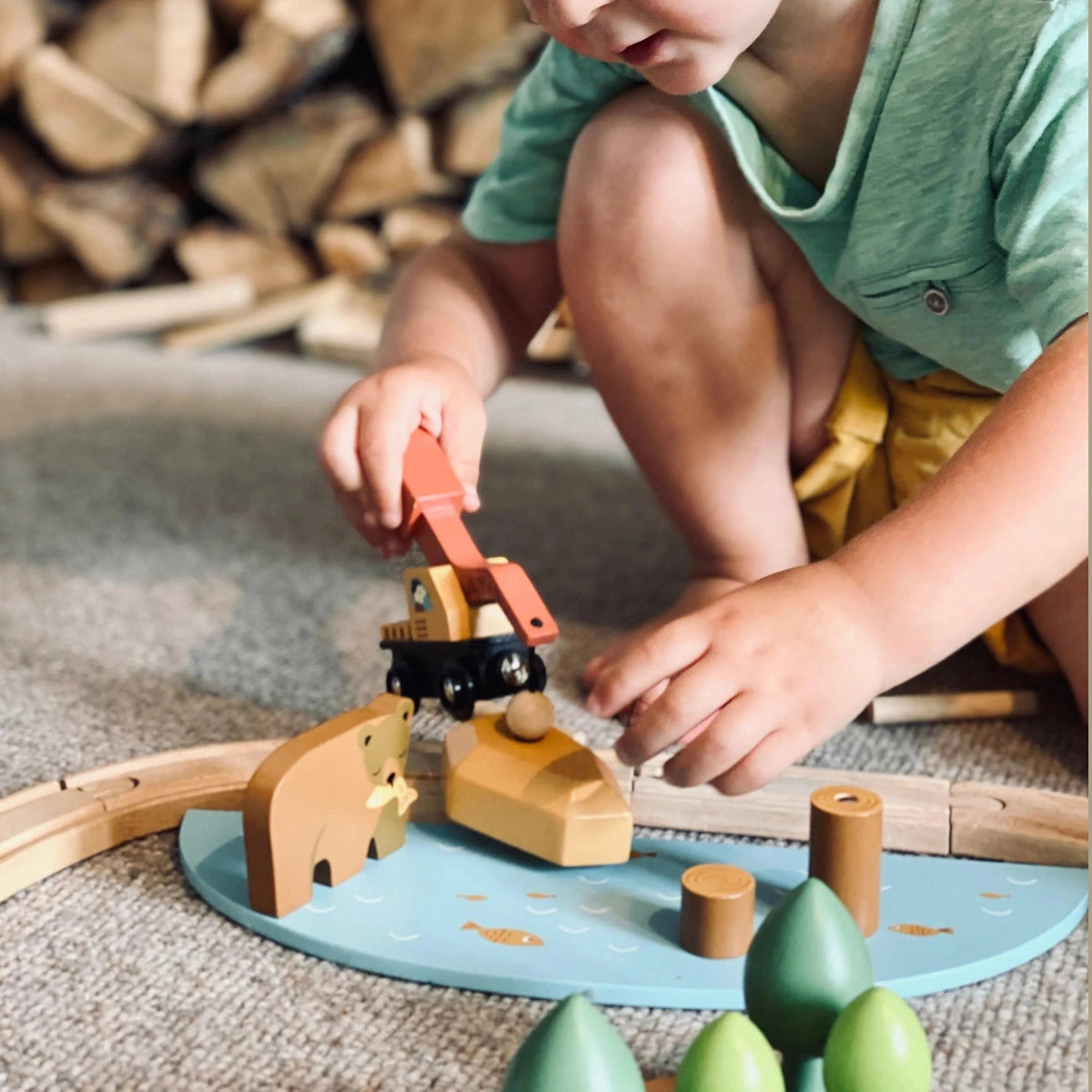 Child playing with a wooden toy train set on the floor.