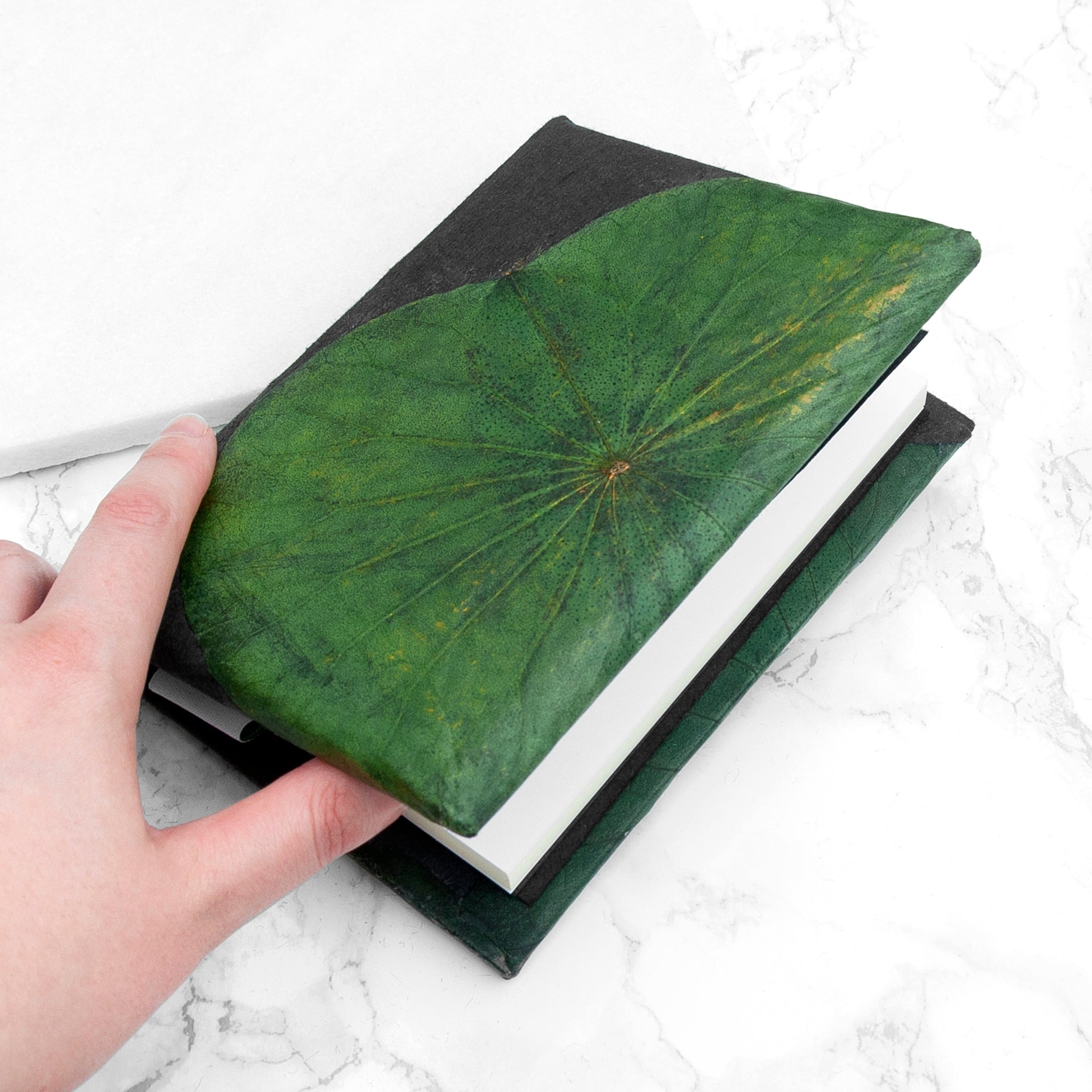 Hand holding a green textured book on a white marble surface