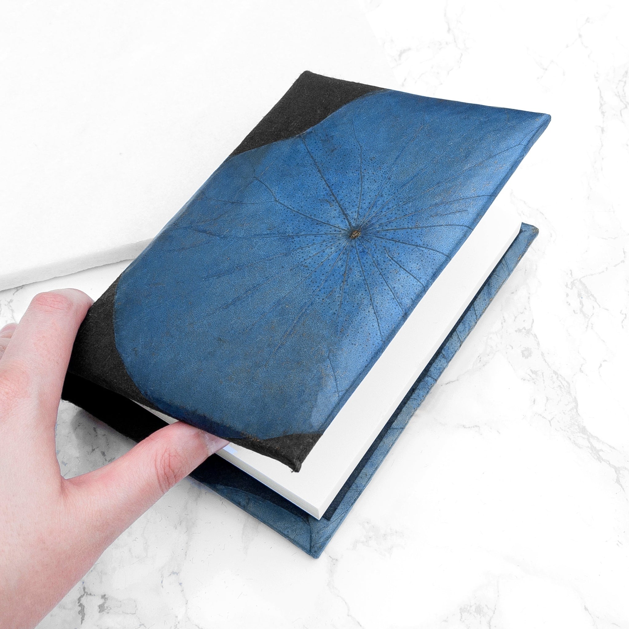 Hand holding a blue and black notebook on a marble surface