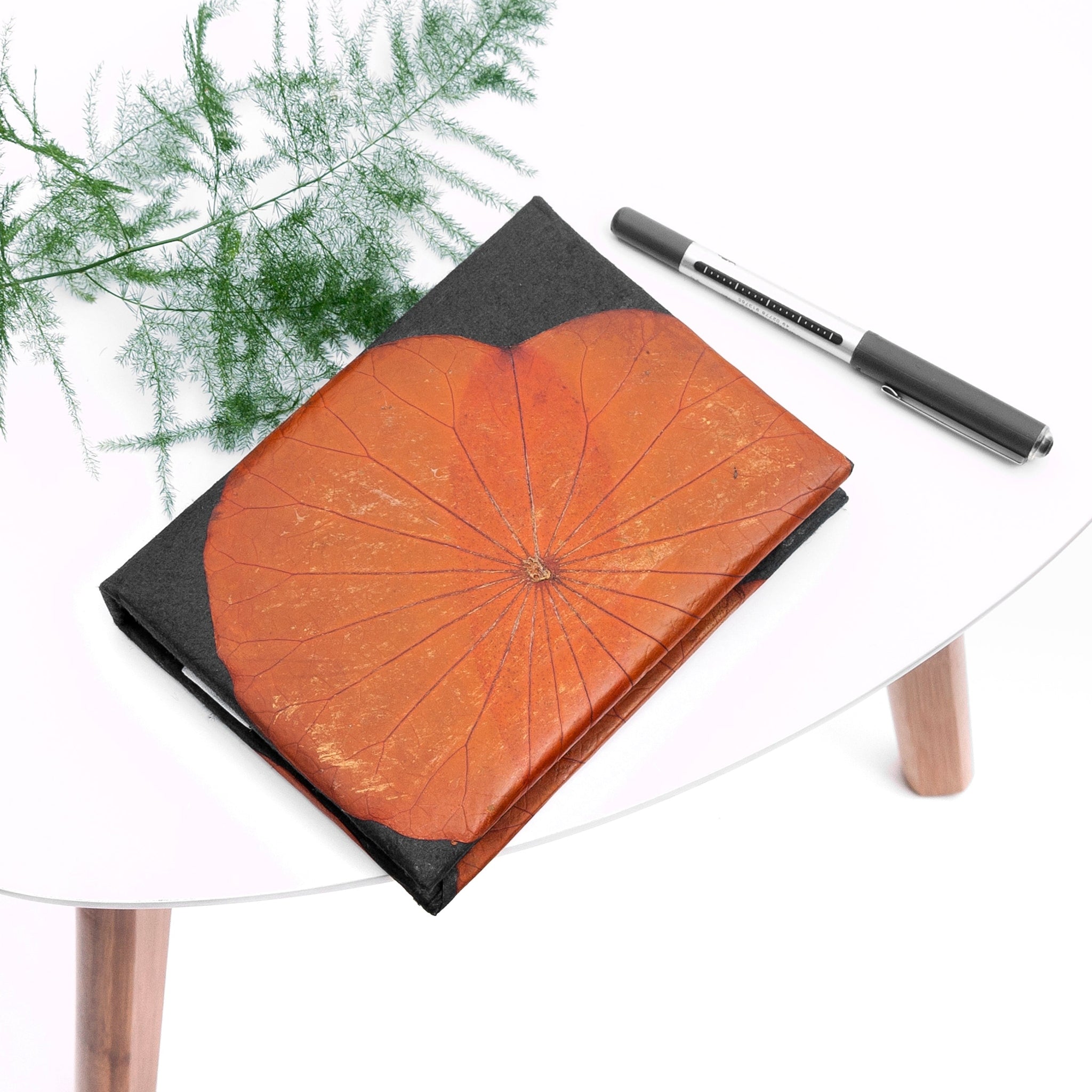 Notebook with orange cover and black edges on a white surface with a pen next to it.