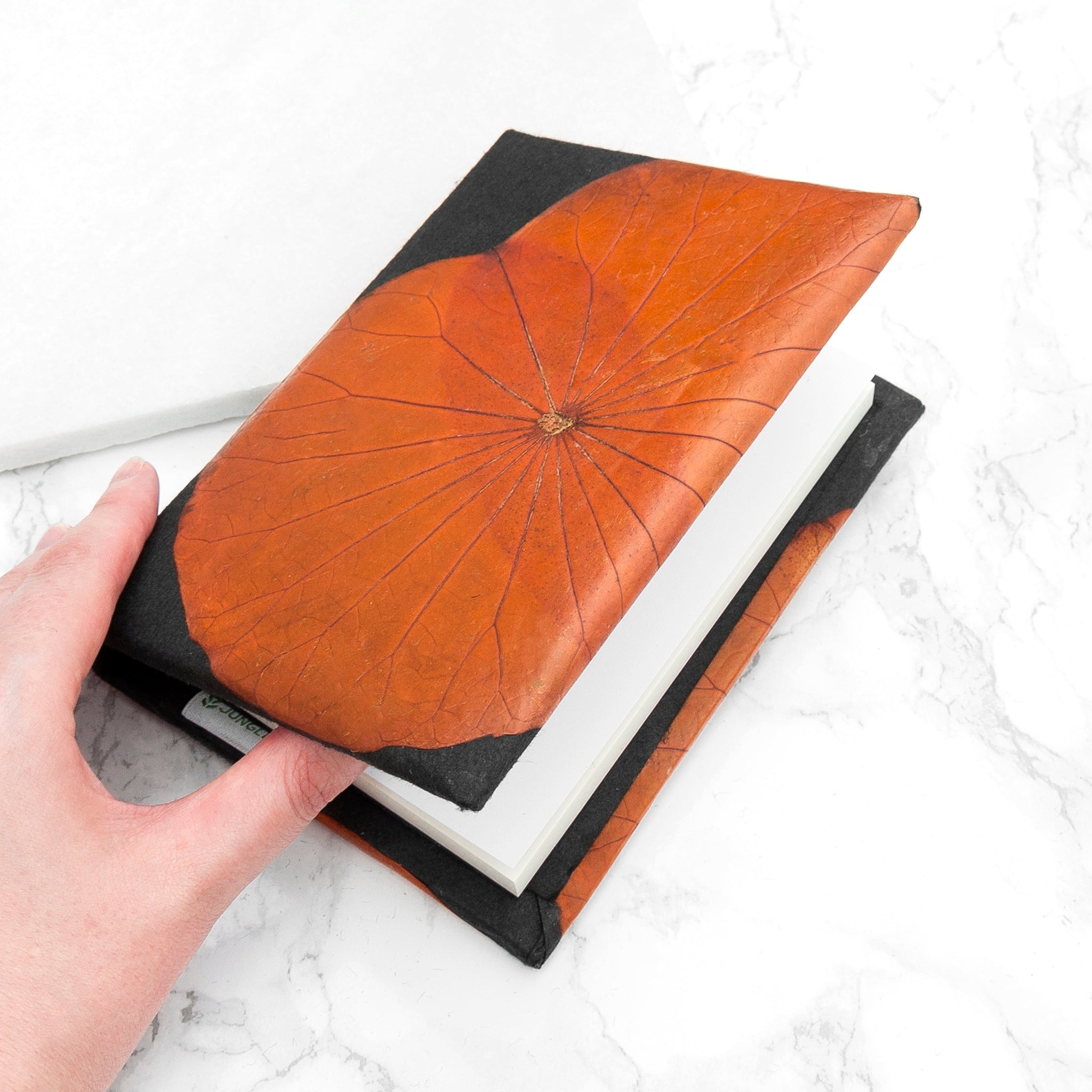 Hand holding a black and orange leather-bound book on a white marble surface